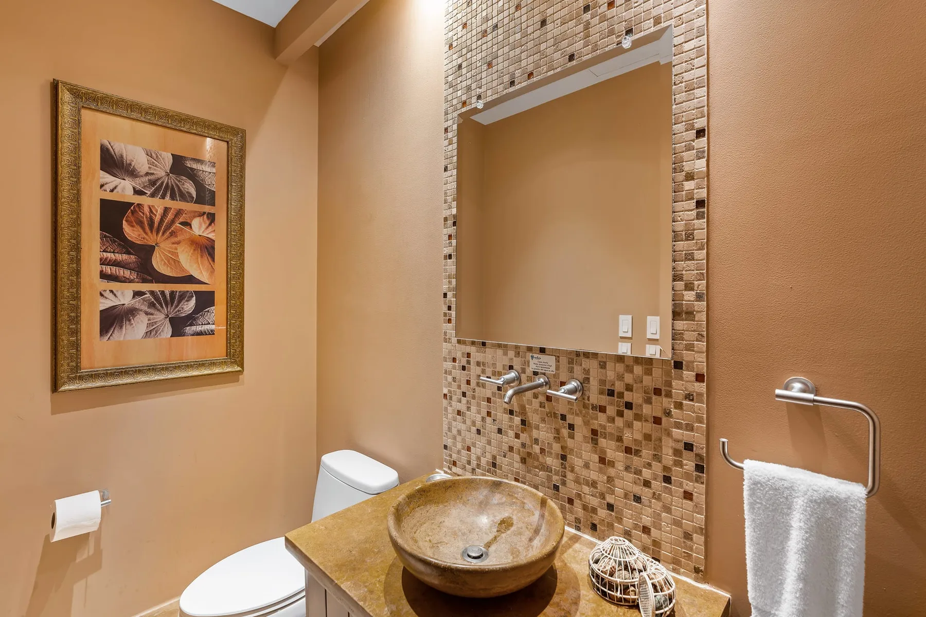 A bathroom with a vessel sink, wall mirror, and framed artwork.