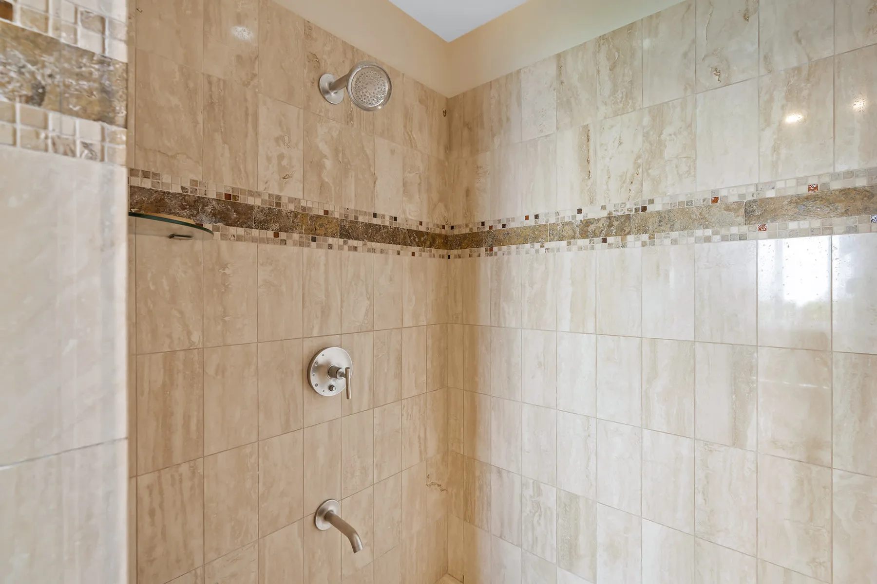 A tiled shower with a decorative mosaic band across the walls.