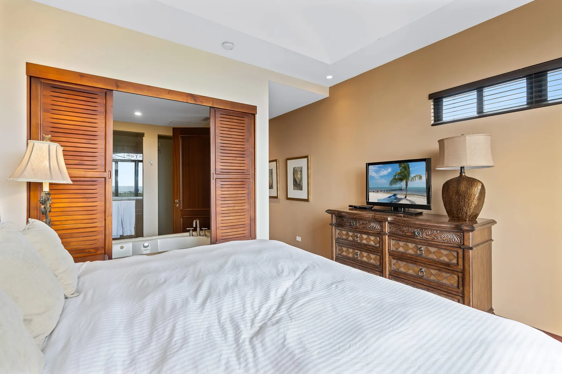 A bedroom with a white bed and wooden sliding doors opening to a bathroom.