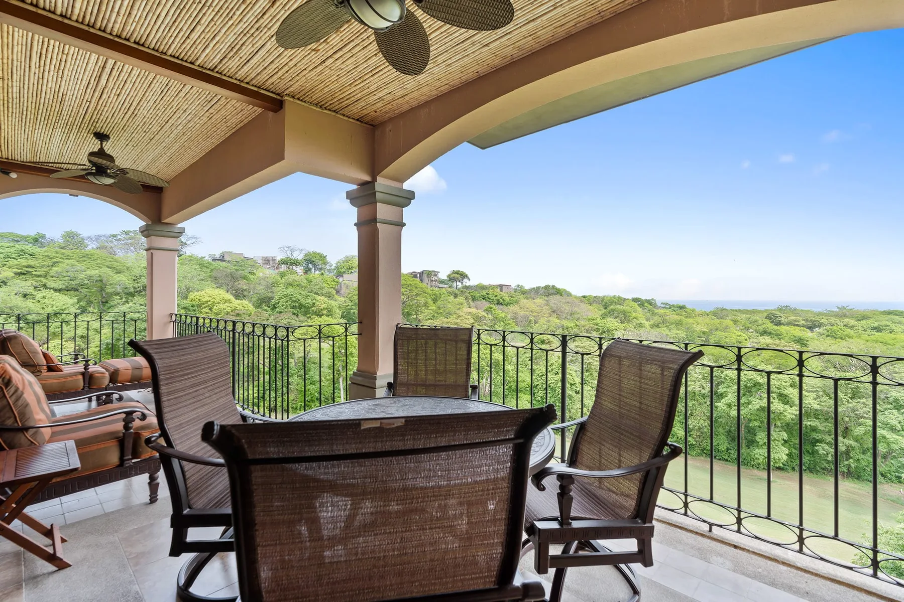 A covered patio with outdoor seating overlooks a green, tree-covered landscape.