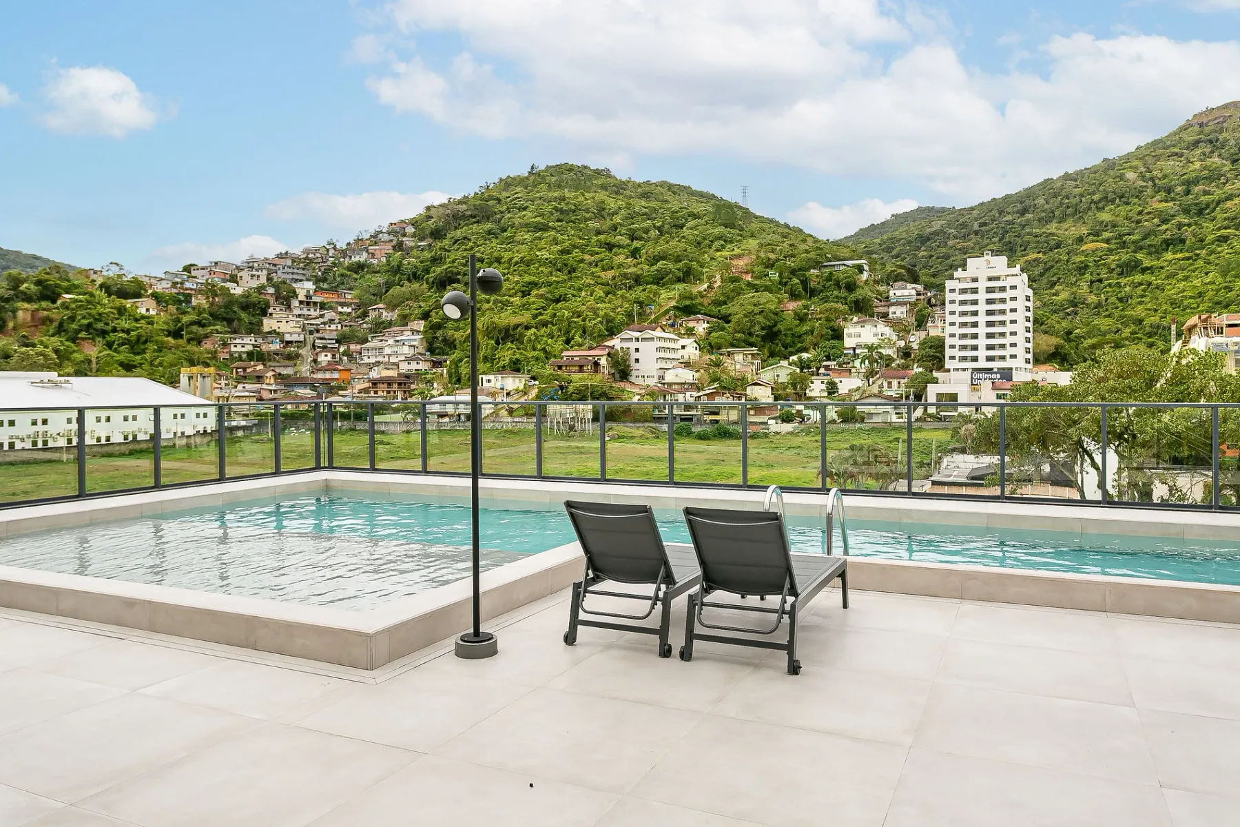 Shared amenity: A rooftop pool and paved terrace overlook green hills and hillside buildings.