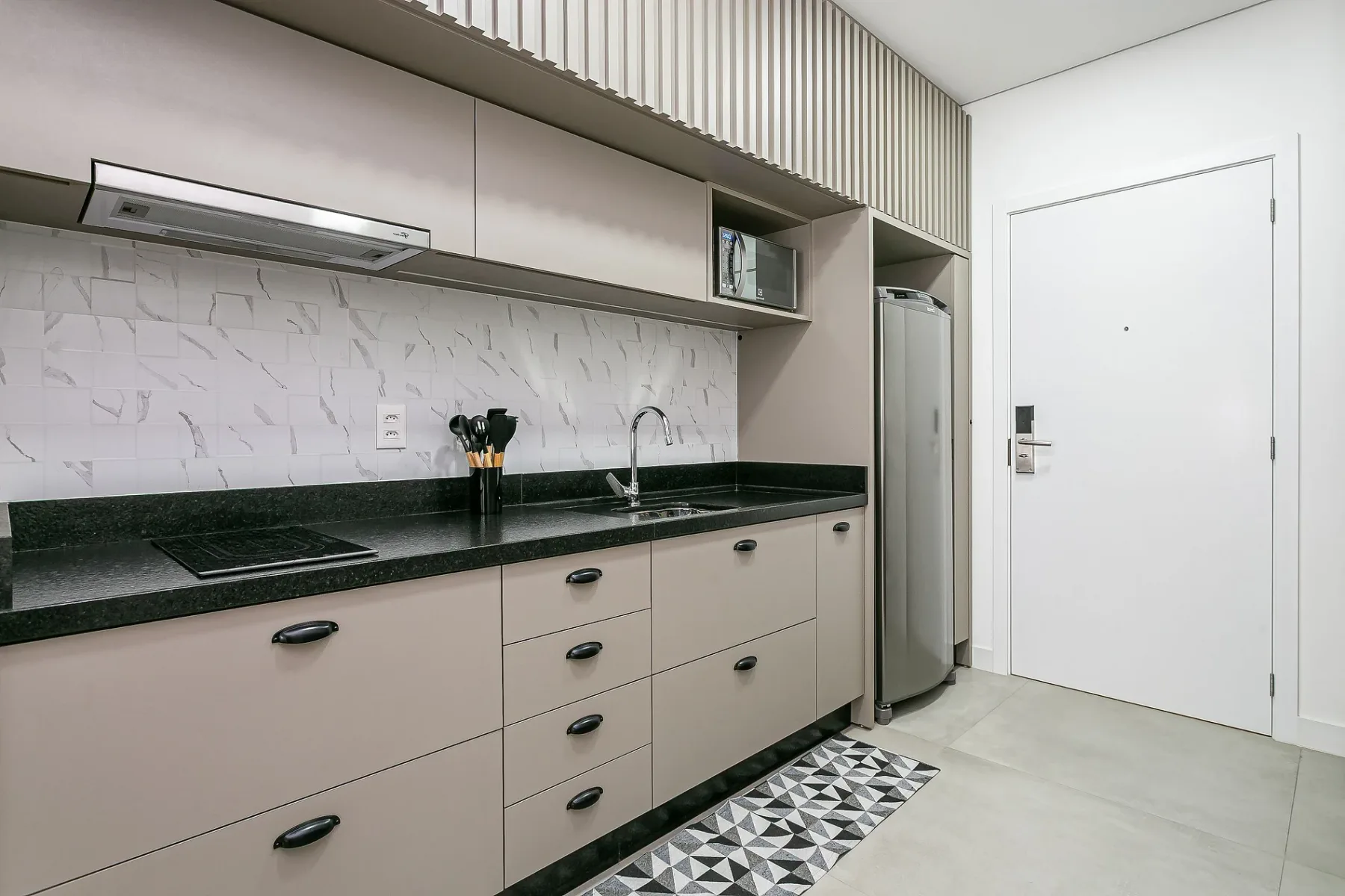 A modern kitchen with light cabinetry, a dark countertop, and a refrigerator.