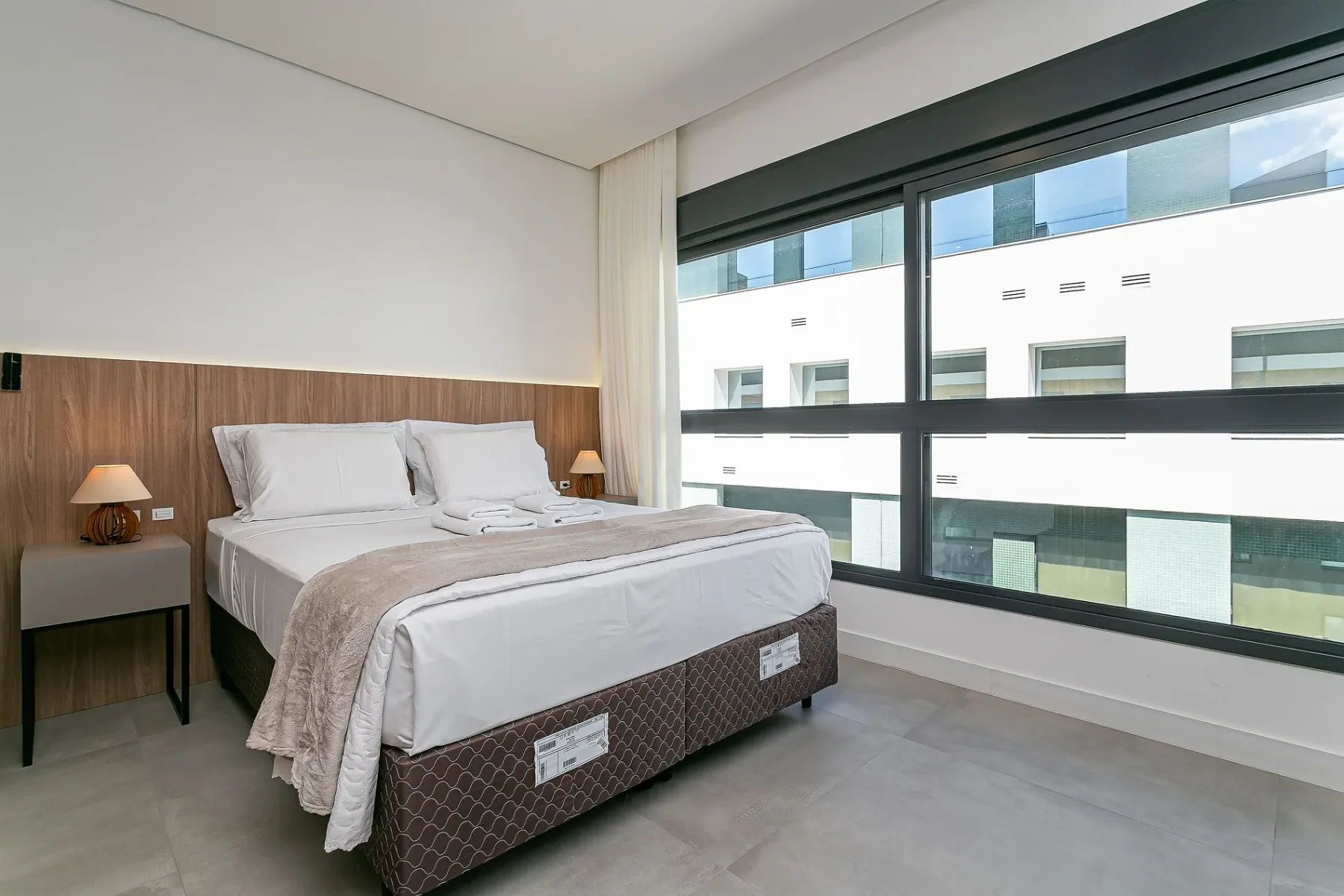 A bright bedroom with a neatly made bed beside a large window.