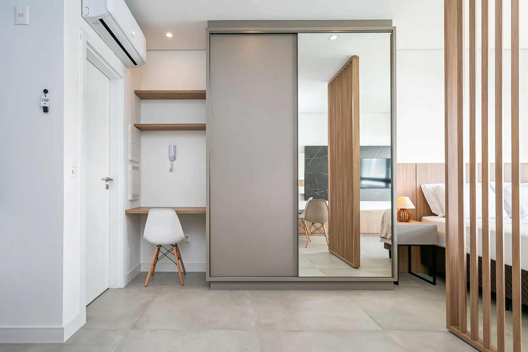 A modern bedroom with a mirrored wardrobe and a small desk.
