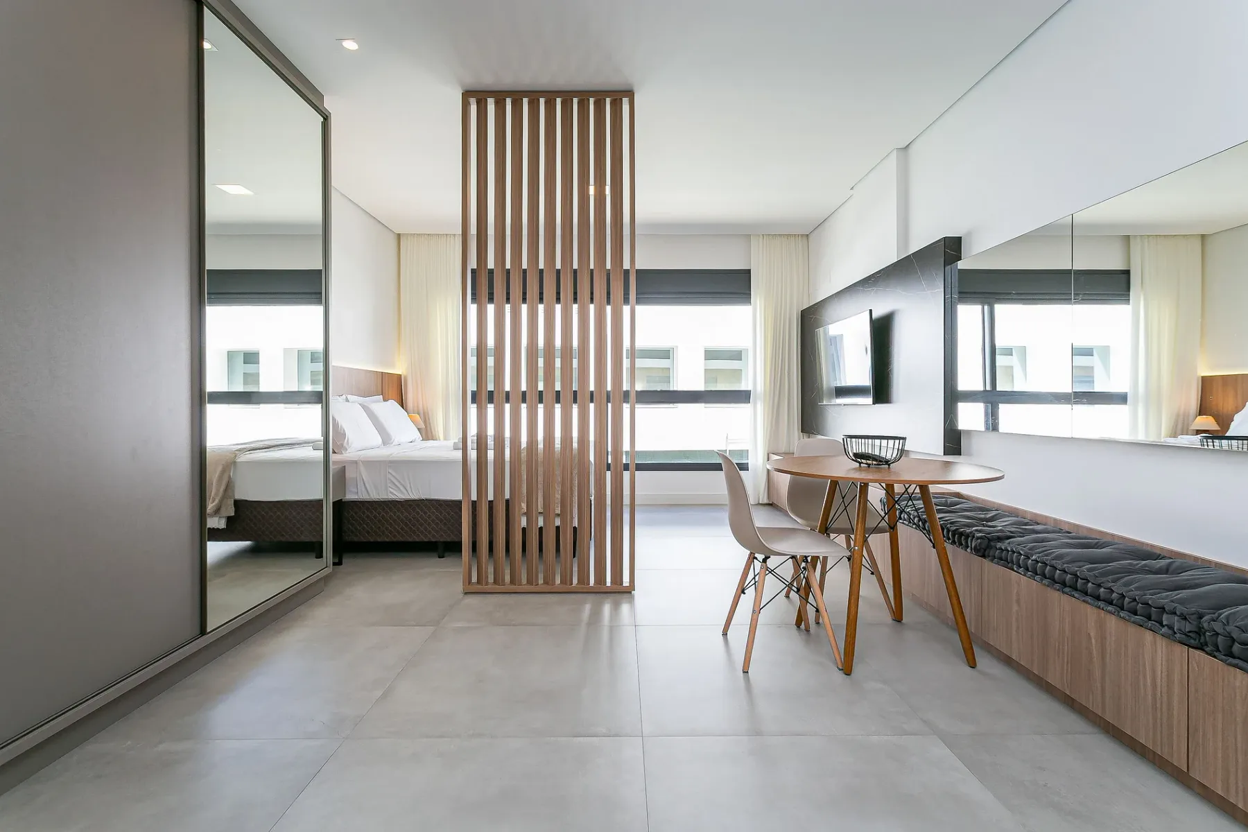 A bright bedroom and sitting area with a bed, dining table, and built-in bench.