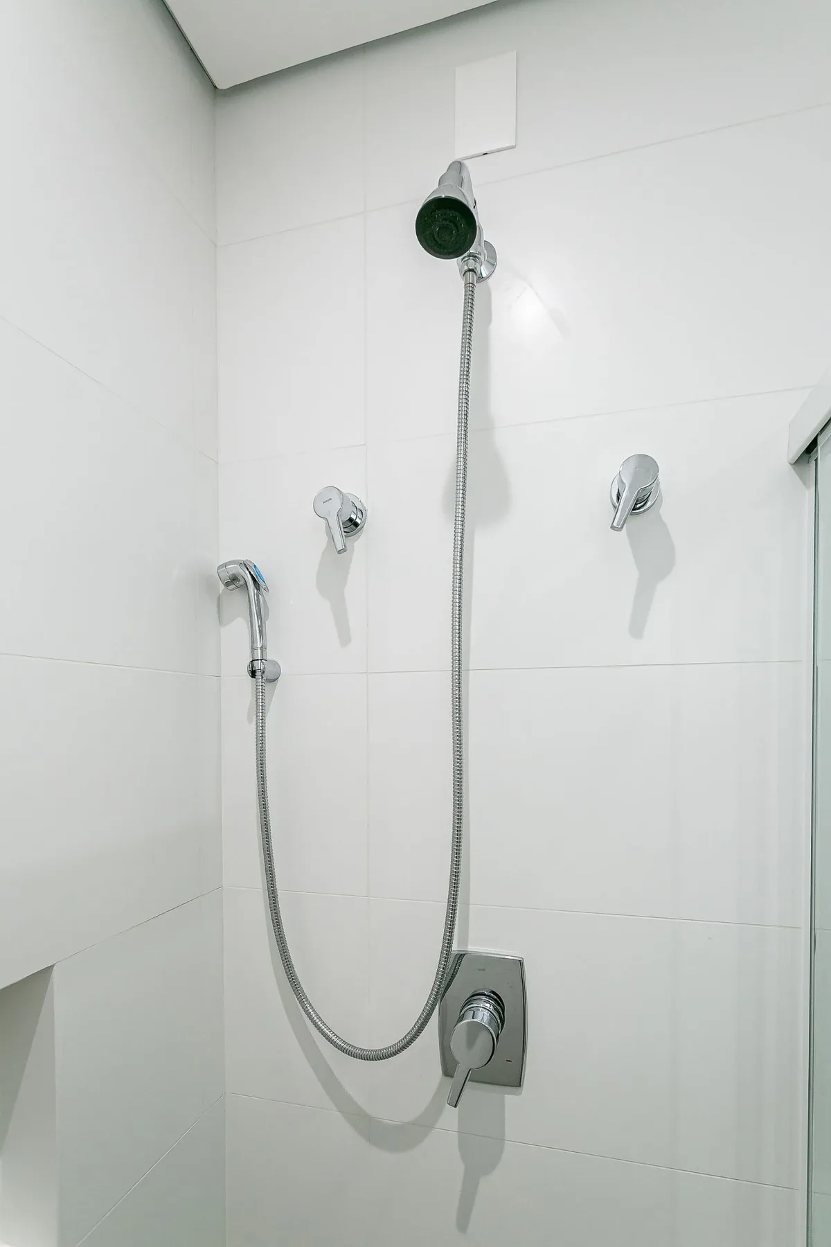 A tiled bathroom shower with a handheld showerhead and wall controls.