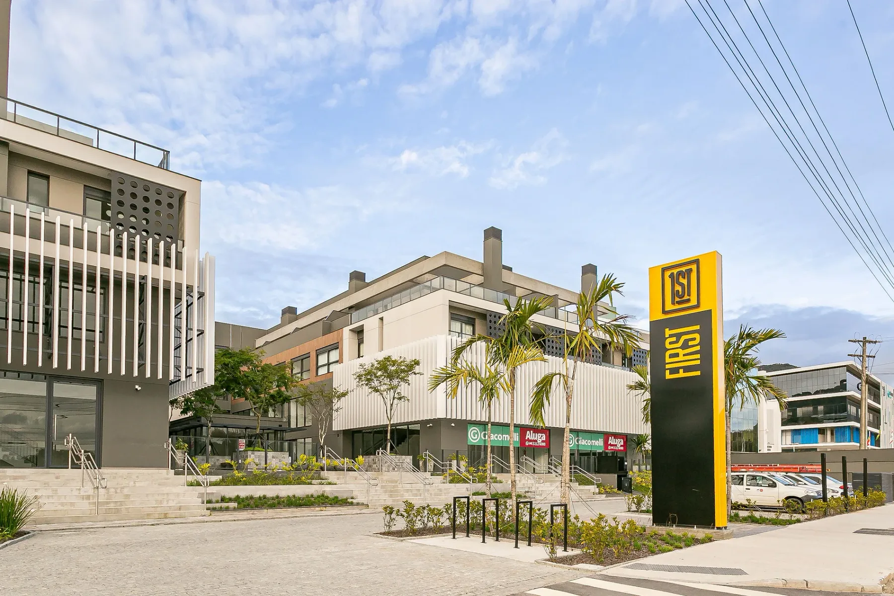 Shared amenity: Street view of a modern commercial building with storefront signs and palm trees.