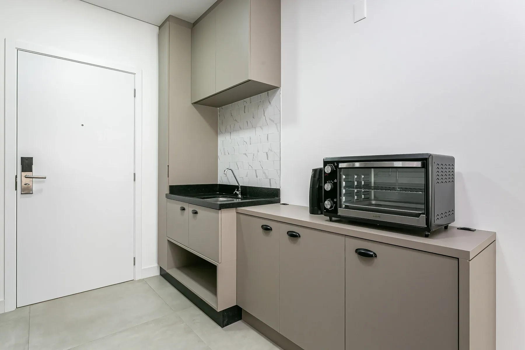 A compact kitchenette with a sink, cabinets, and a countertop oven.