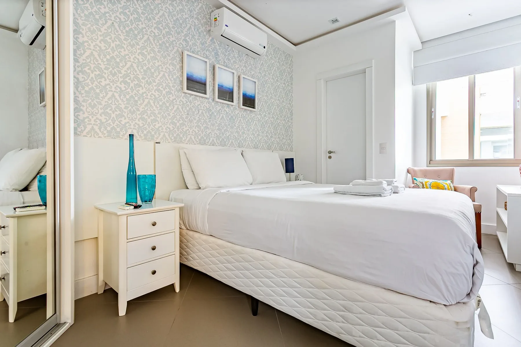 A bright bedroom with a large bed, framed pictures, and a window.