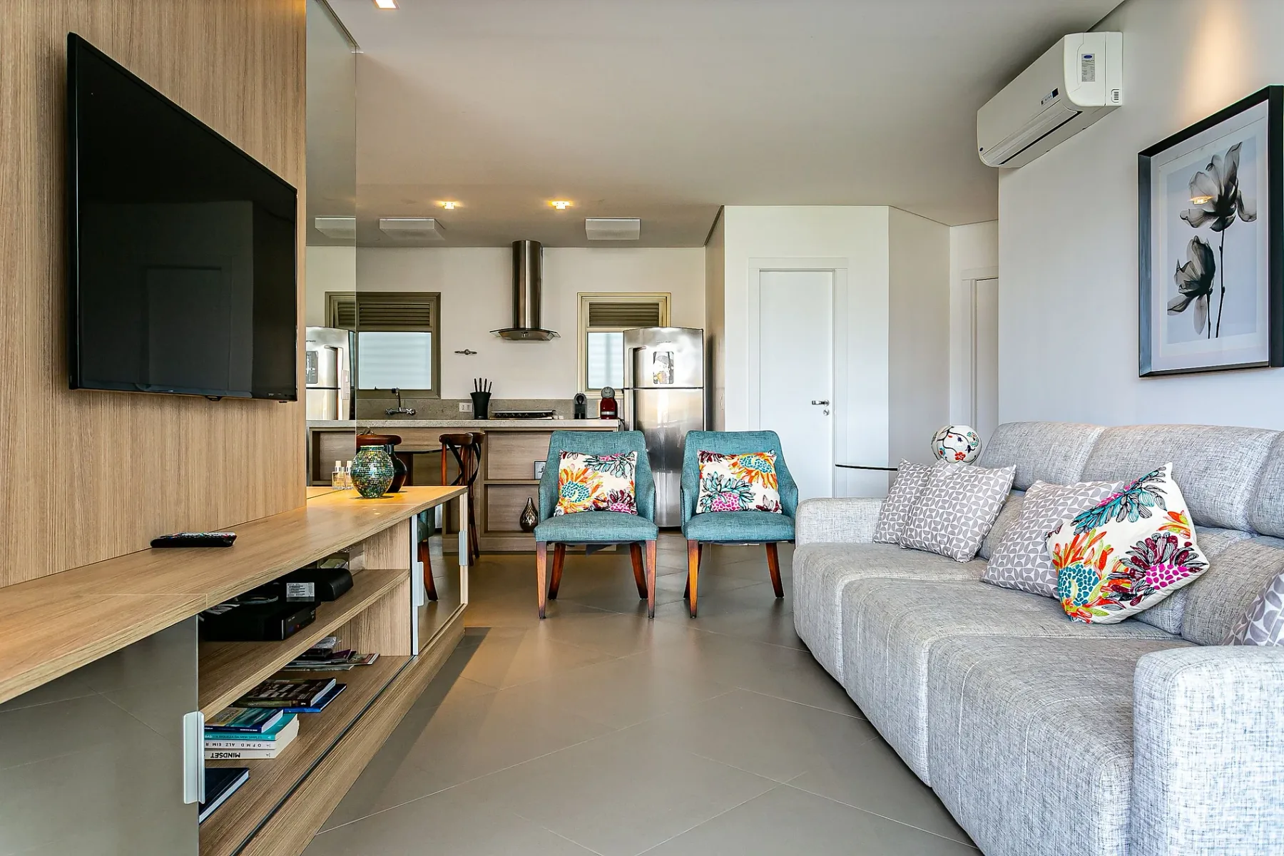 A living room with a television, seating, and a kitchen area in the background.
