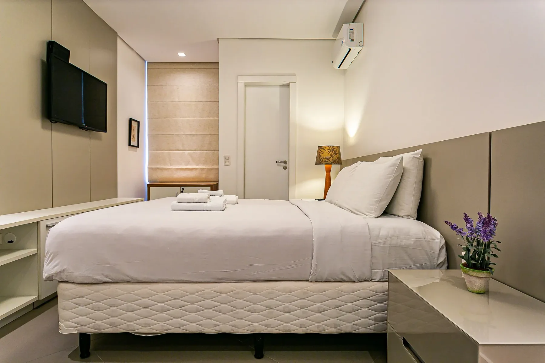 A bedroom with a neatly made bed and a wall-mounted television.