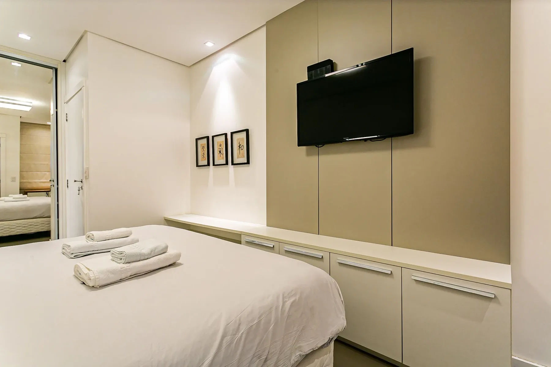 A bedroom with a neatly made bed and a wall-mounted television.