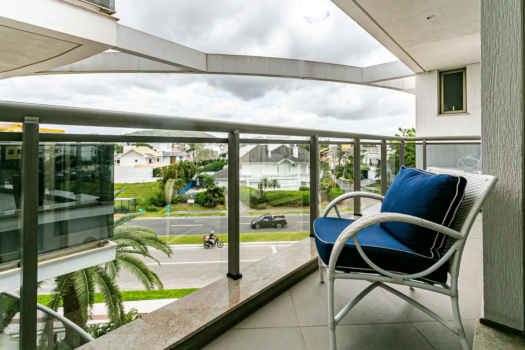 A balcony with blue-cushioned seating overlooks a street and nearby buildings.
