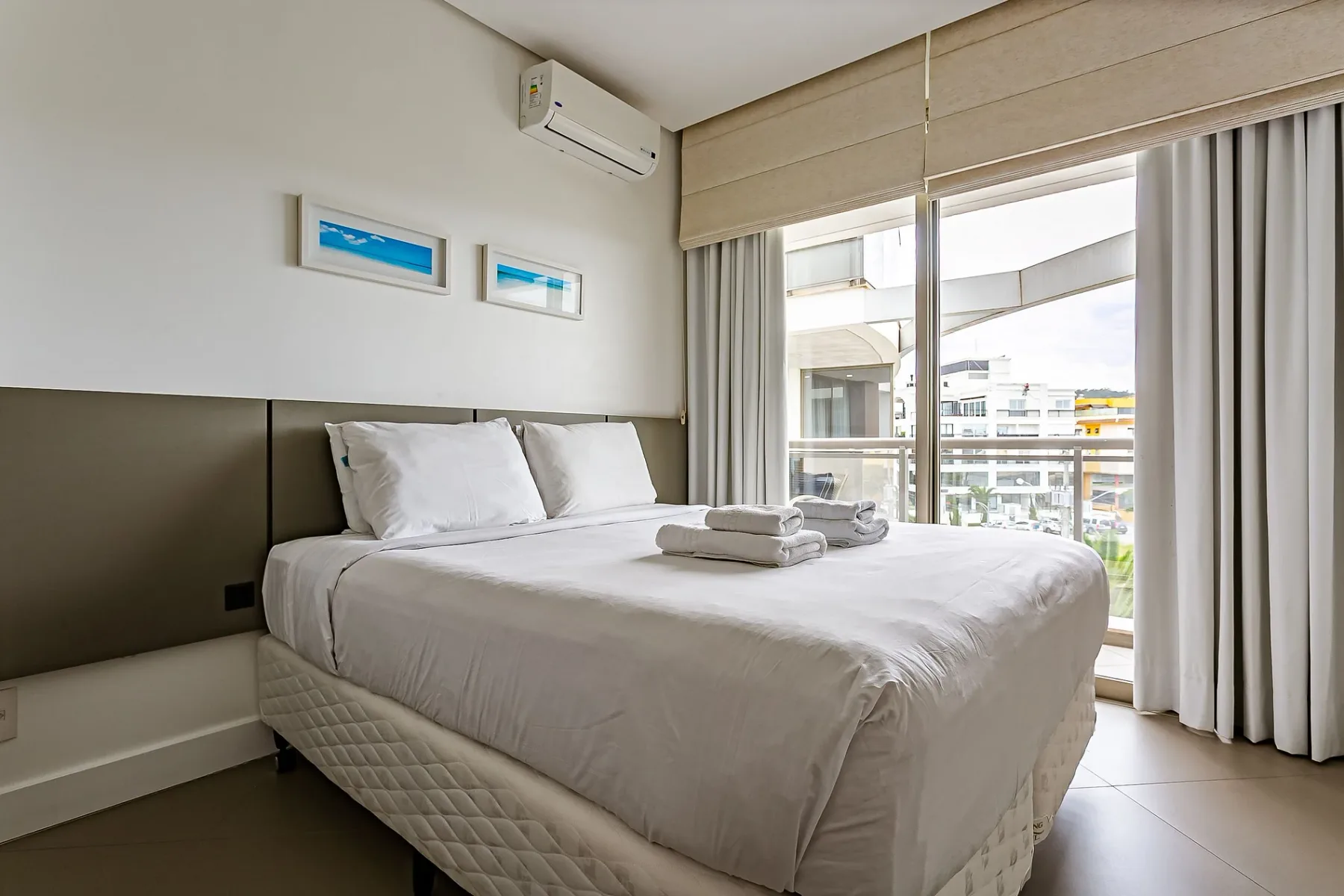 A bright bedroom with a neatly made bed beside large windows.