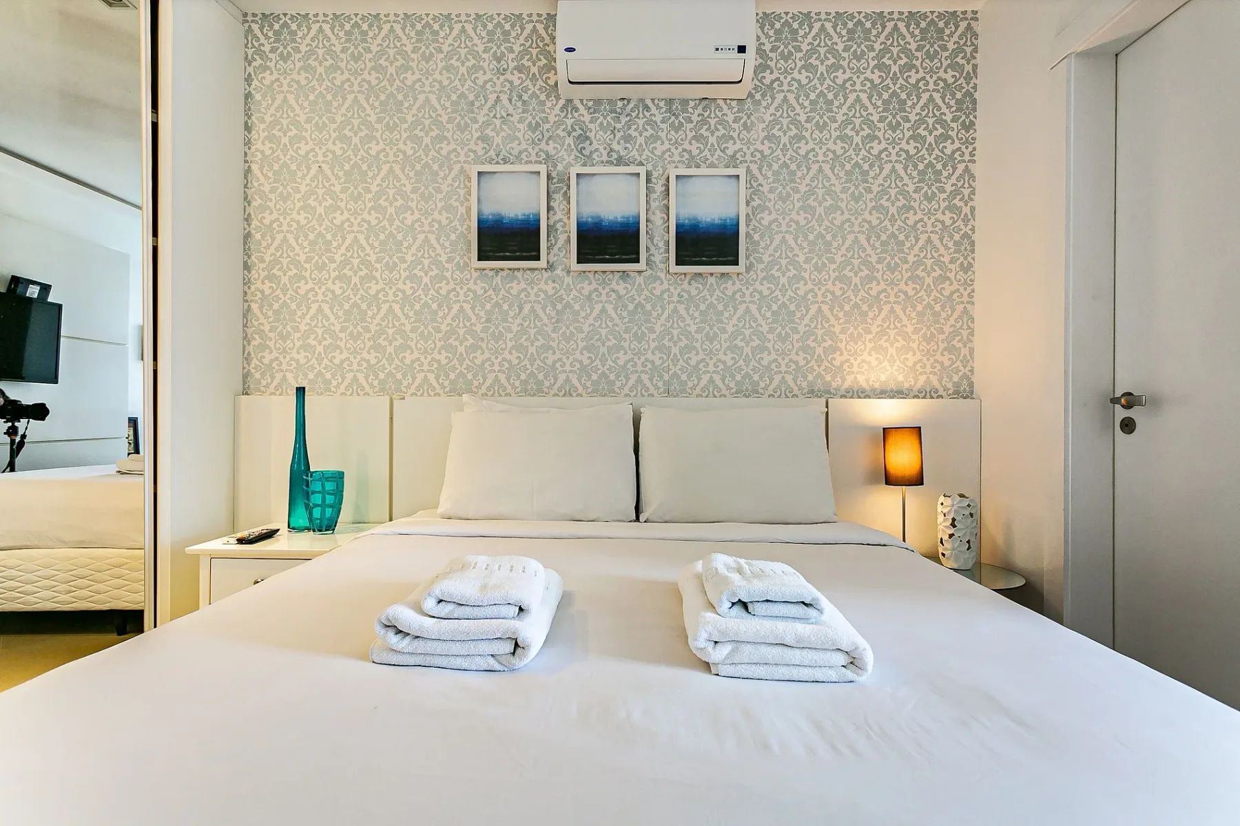 A bedroom with a neatly made bed, patterned wallpaper, and bedside lamps.