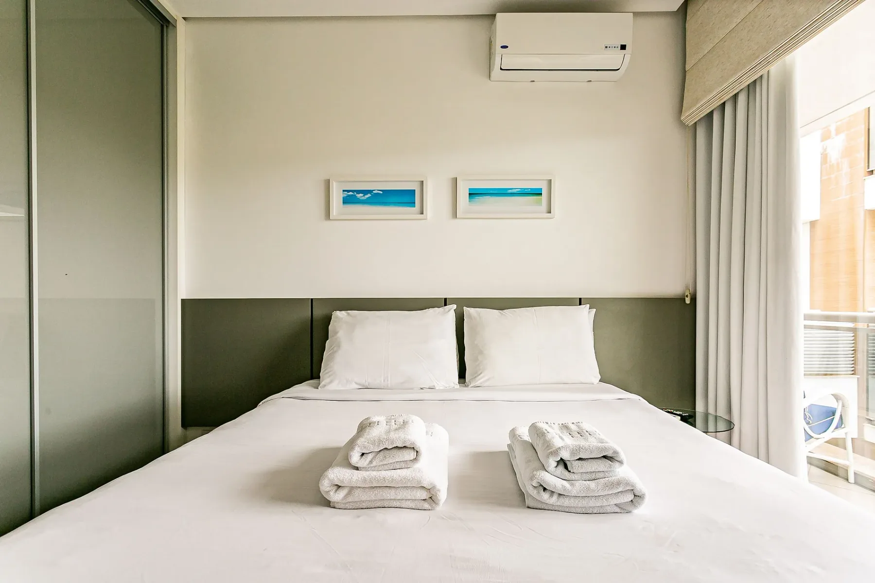 A bedroom with a neatly made bed and folded towels at the foot.