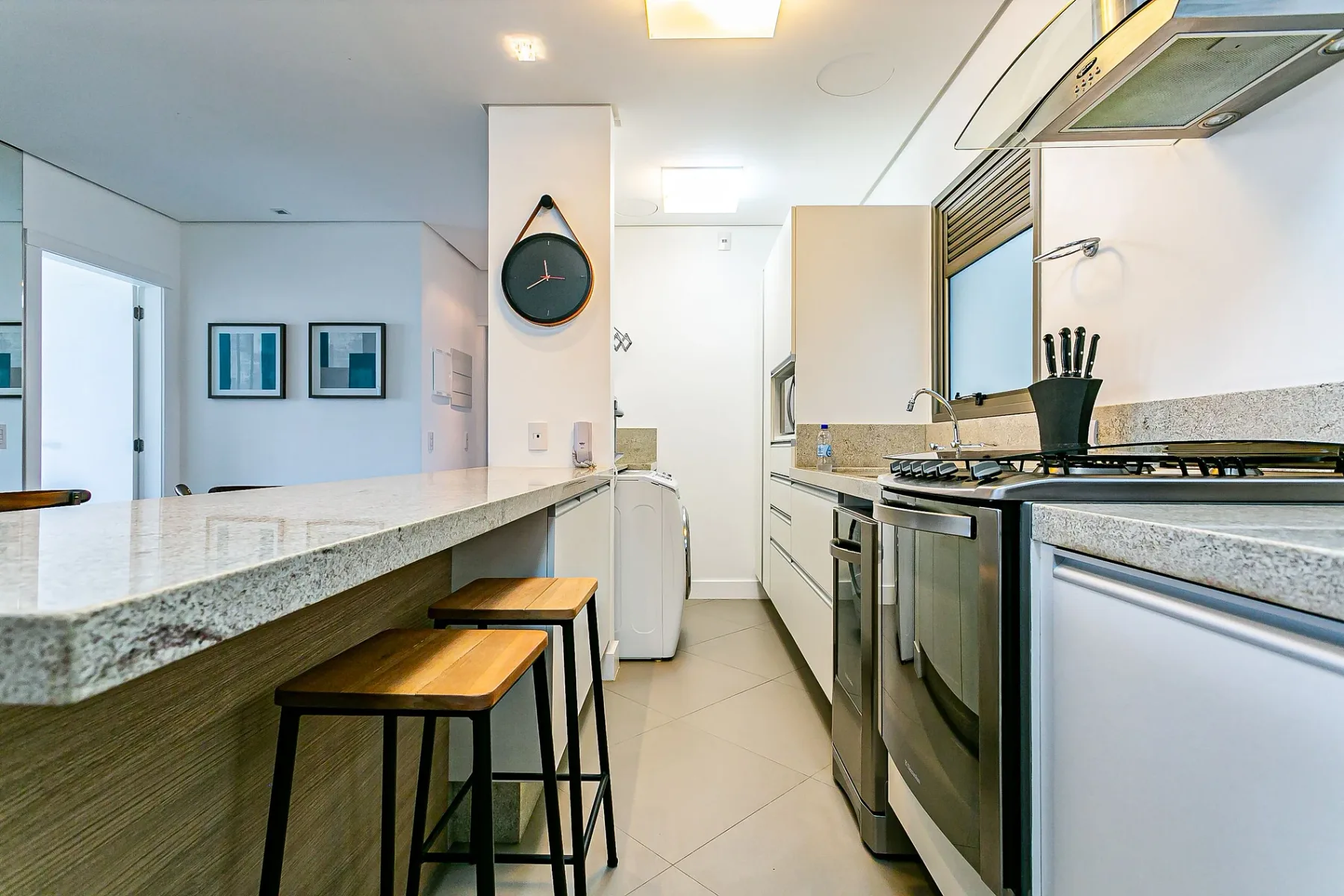 A modern kitchen with a long counter, stools, and cooking appliances.