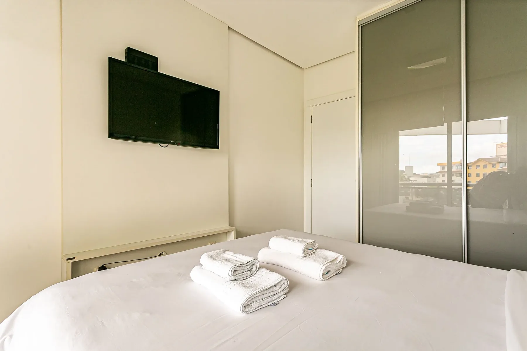 A bright bedroom with a neatly made bed and a wall-mounted television.