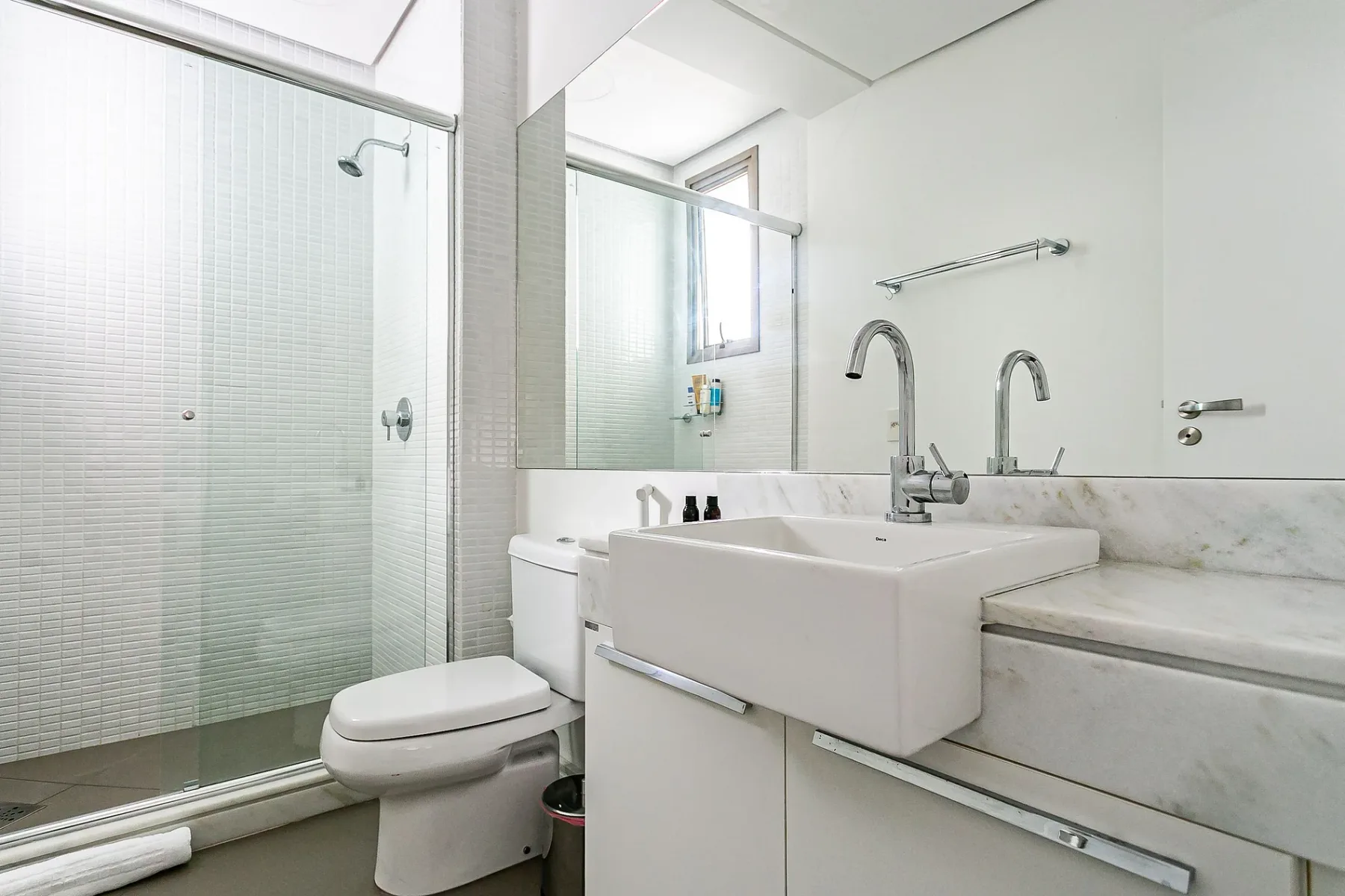 A bright bathroom with a shower, toilet, and a large sink beneath a mirror.