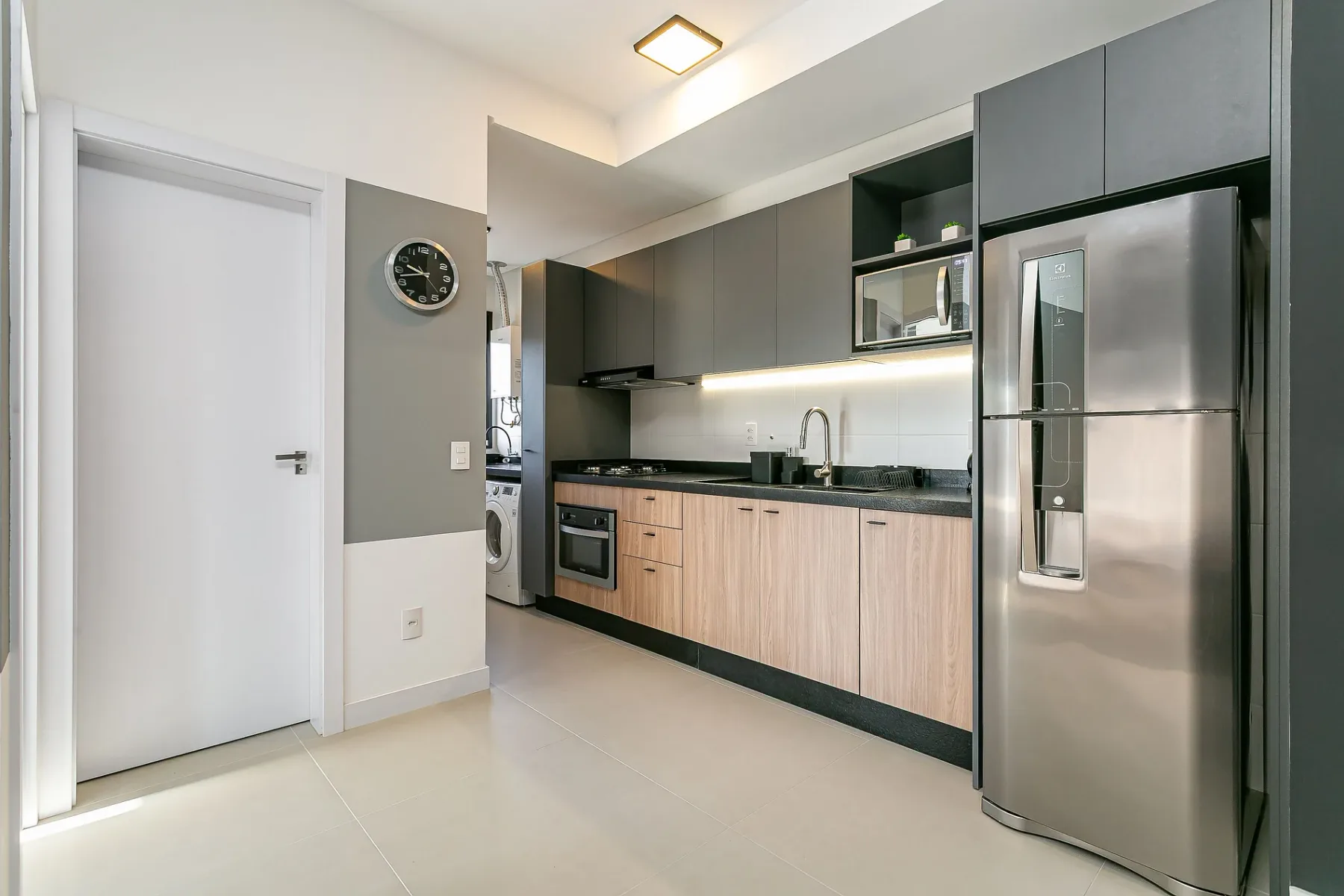 A modern kitchen with wood-toned cabinets, dark countertops, and a stainless steel refrigerator.