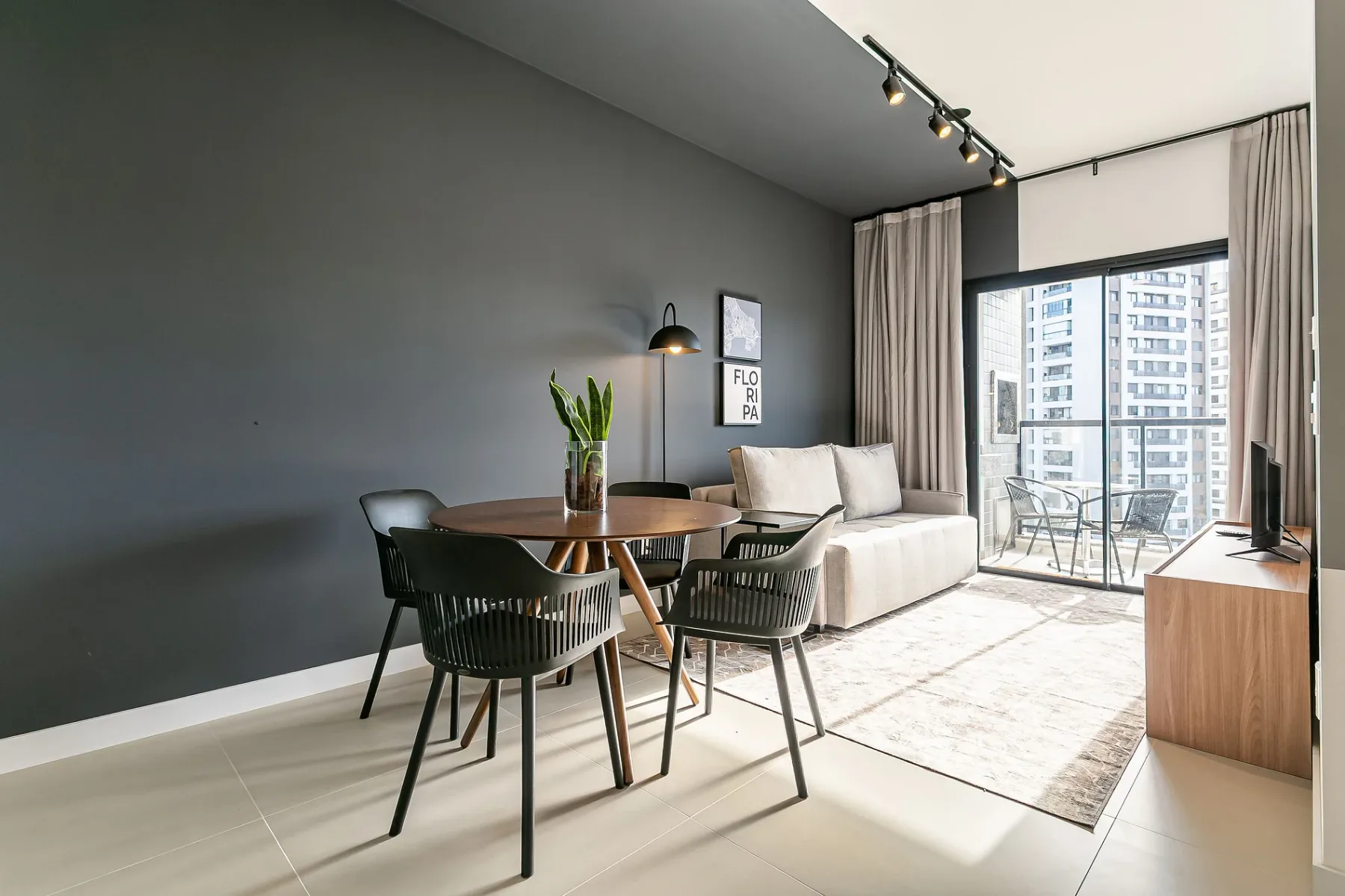 A bright living and dining area with a round table, seating, and large windows.