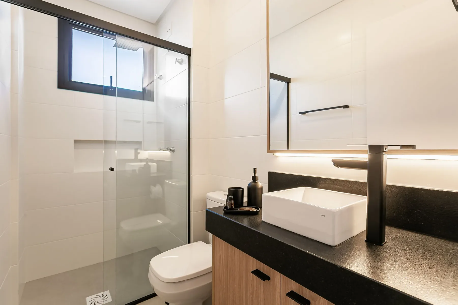 A bathroom with a glass shower, toilet, and sink on a dark counter.