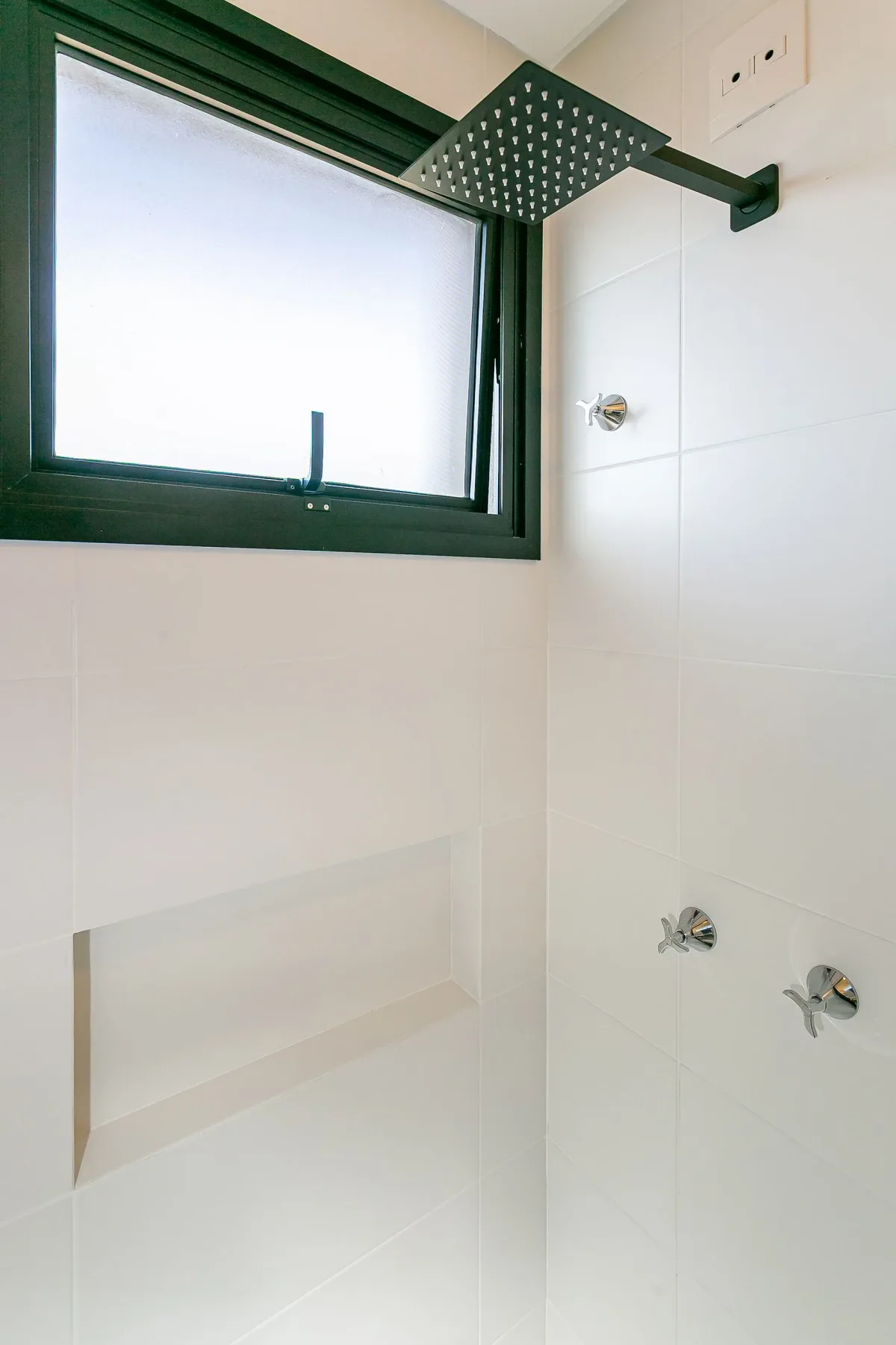 A tiled shower area with a high window and a recessed wall shelf.