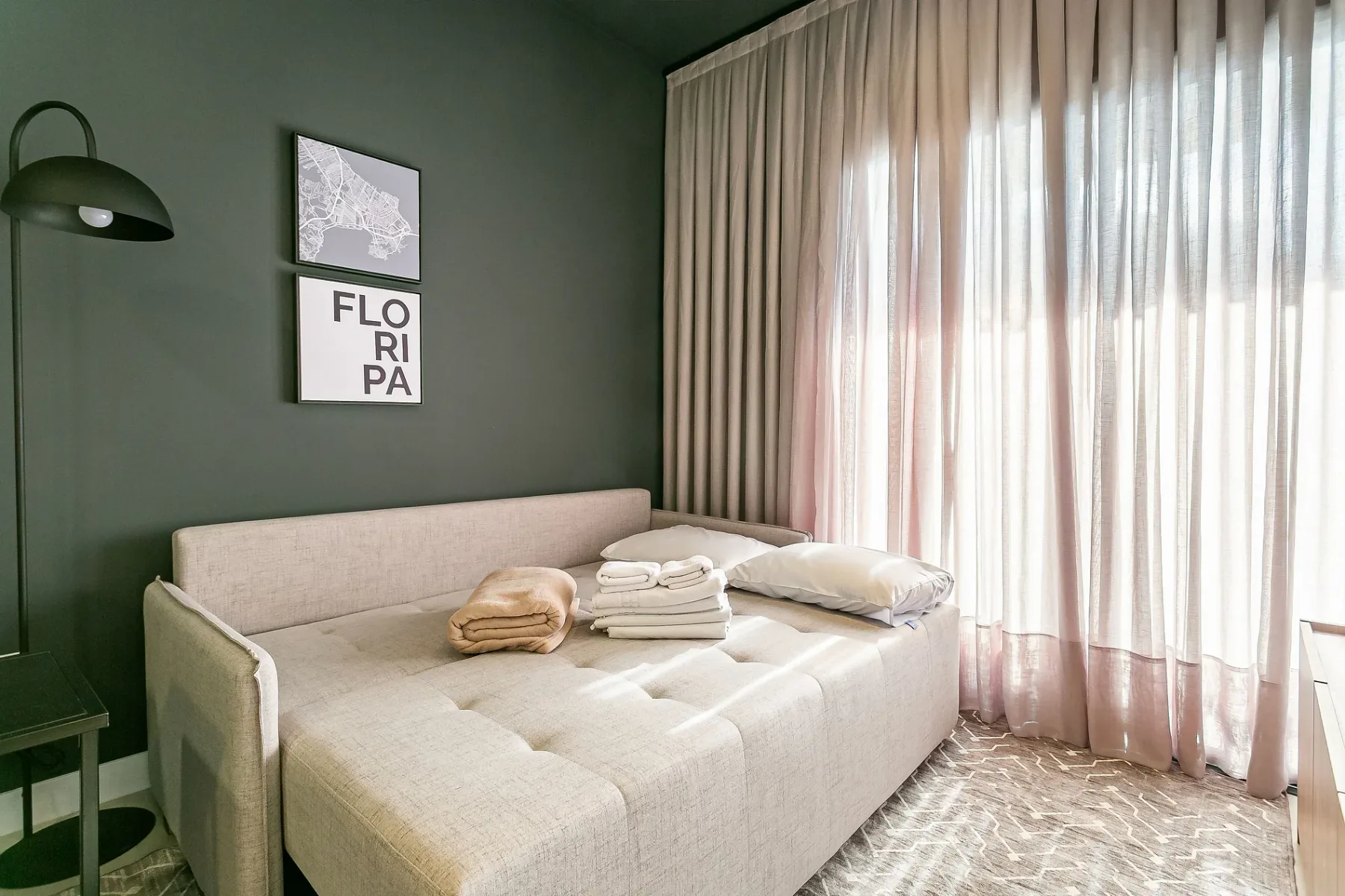 A bright sitting area with a beige daybed beside floor-length curtains.