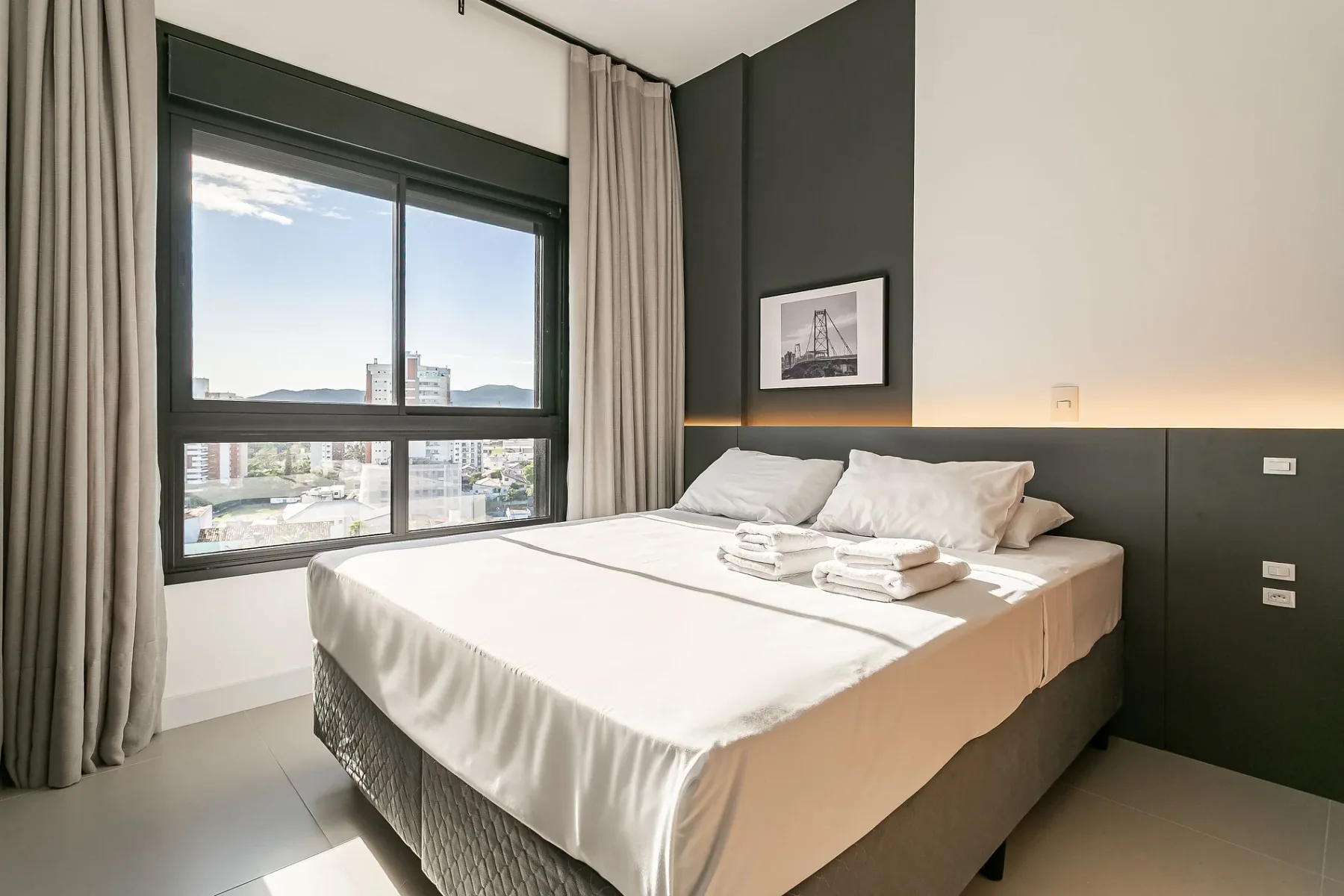 A bedroom with a neatly made bed beside a large window.