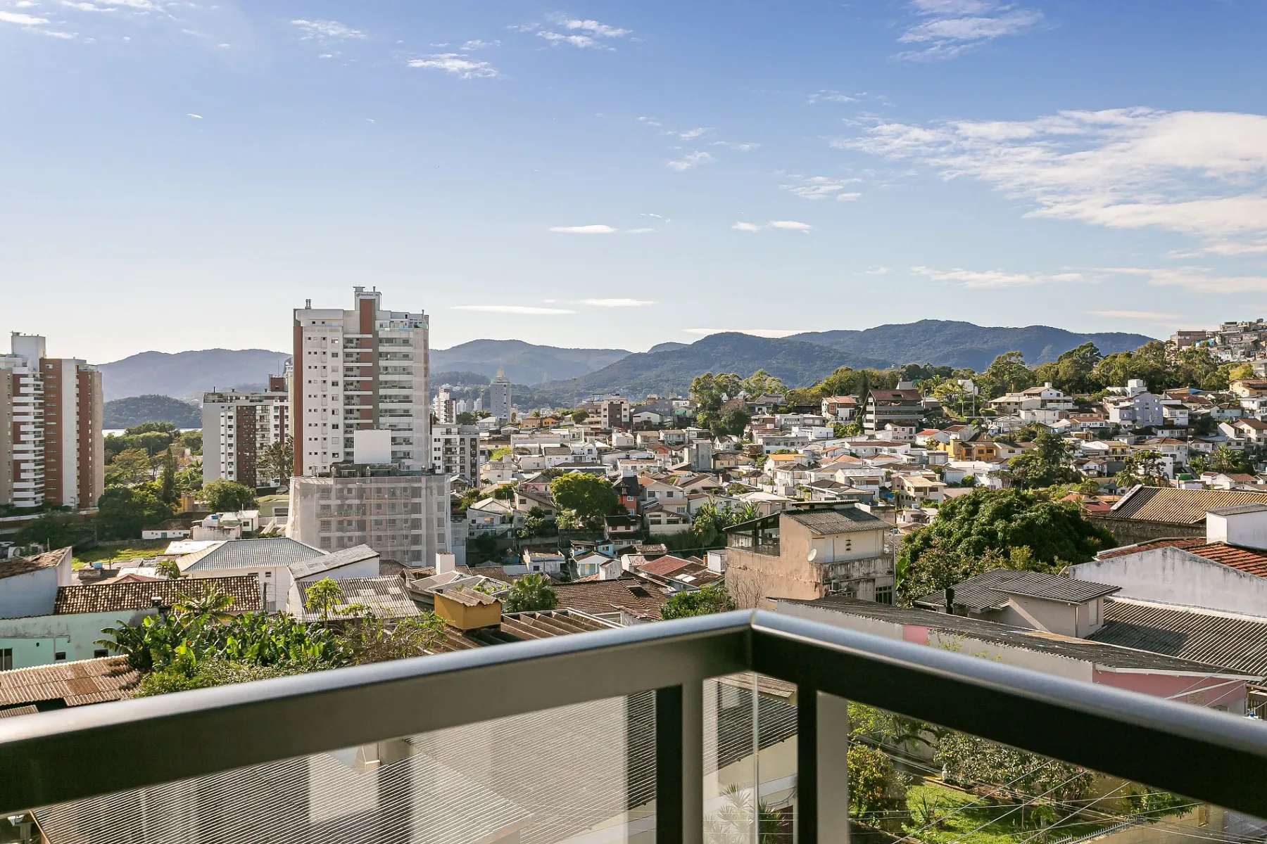 A cityscape viewed from a balcony, with hills in the distance.
