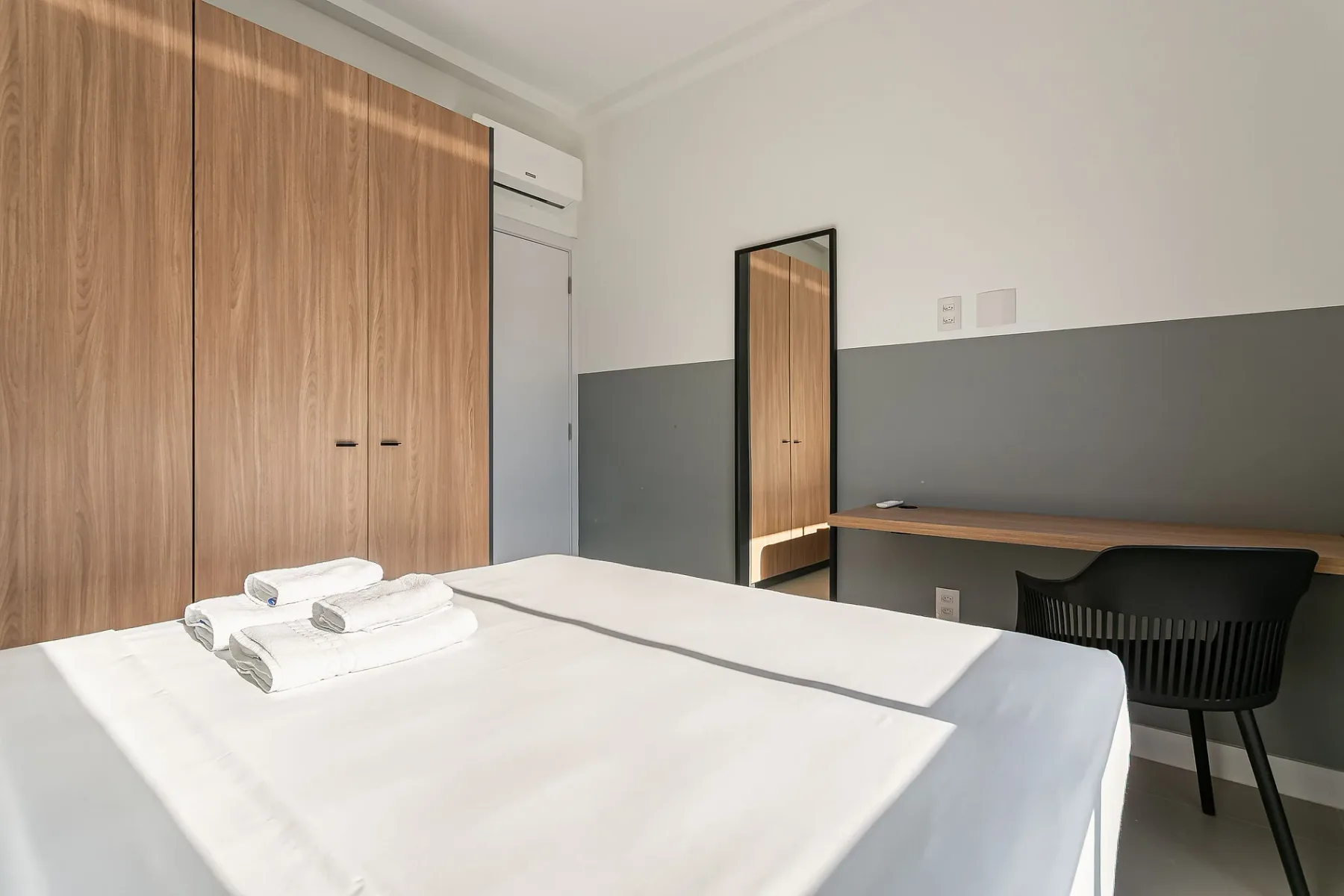 A bedroom with a neatly made bed, towels, and a desk.