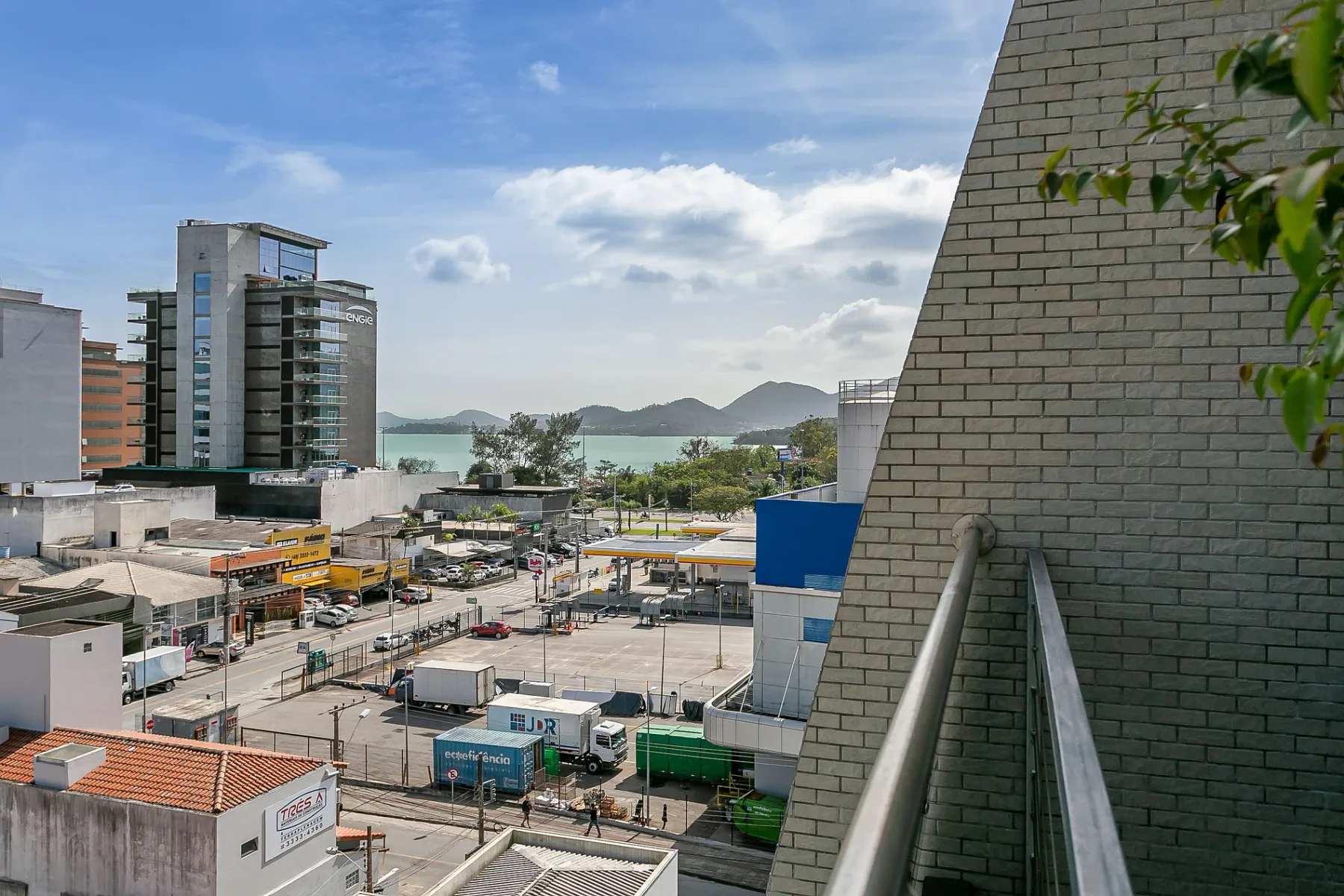 An urban waterfront view with buildings, a busy road, and distant hills.