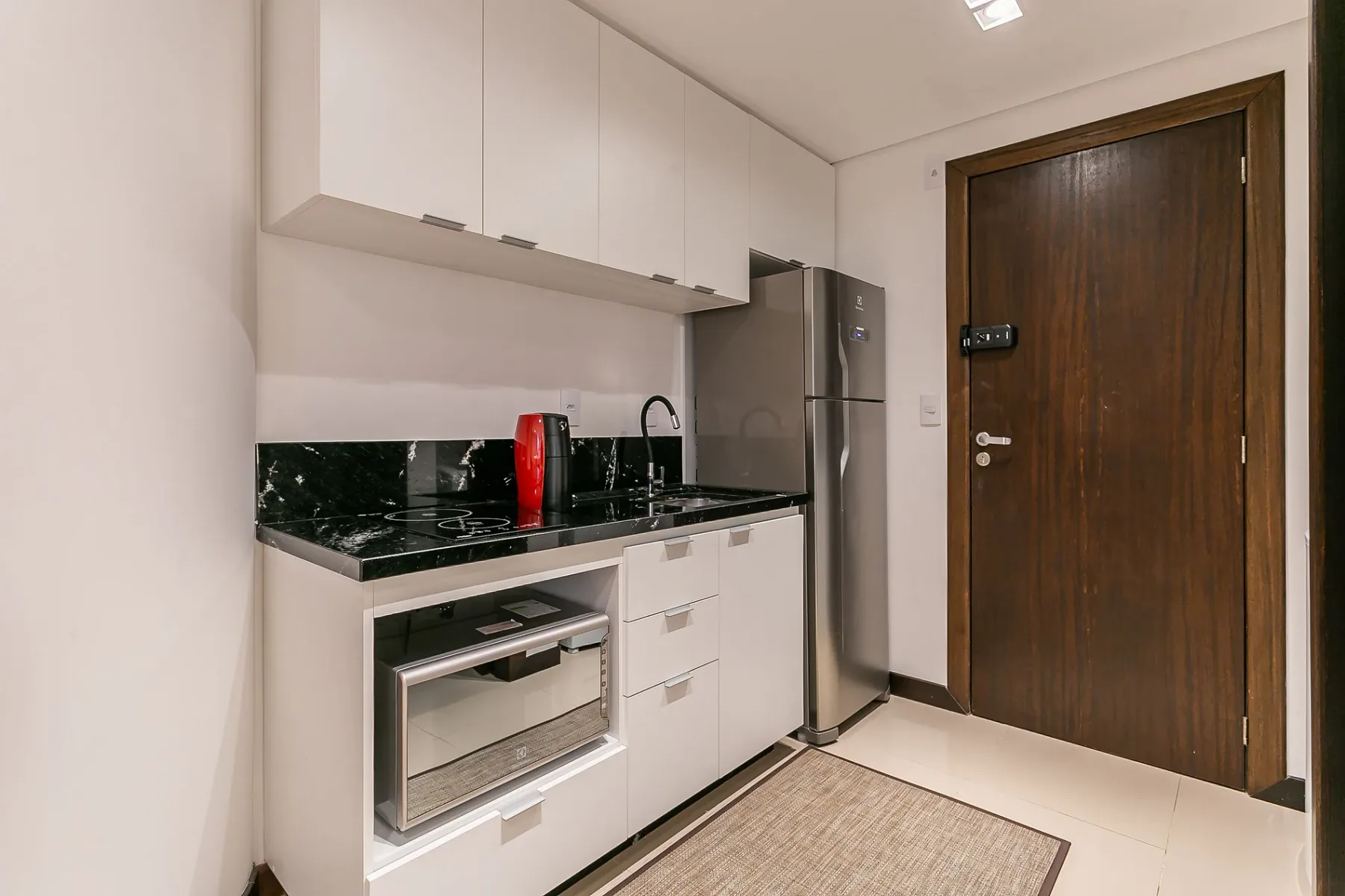 A compact kitchen with white cabinets, dark counters, and a stainless-steel refrigerator.