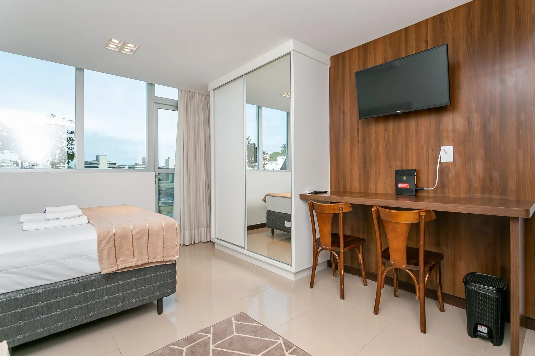 A bright bedroom with a bed, large windows, and a wooden desk.