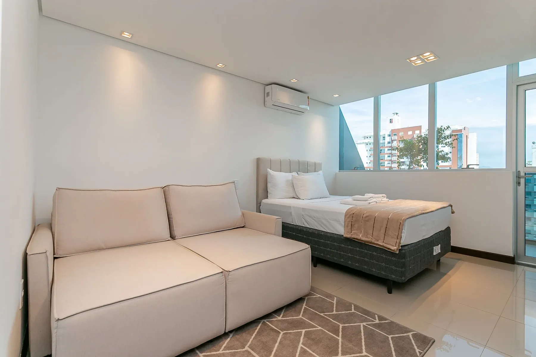 A bedroom with a bed, a sofa, and large windows.