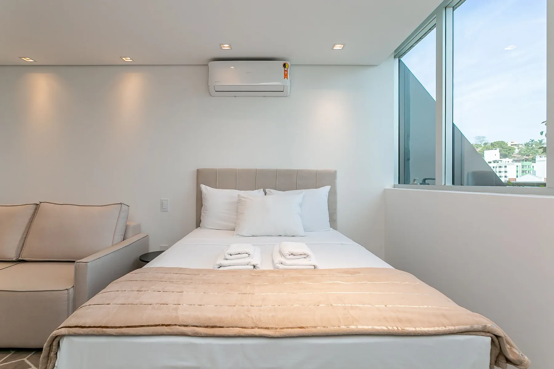 A bright bedroom with a neatly made bed beside large windows.