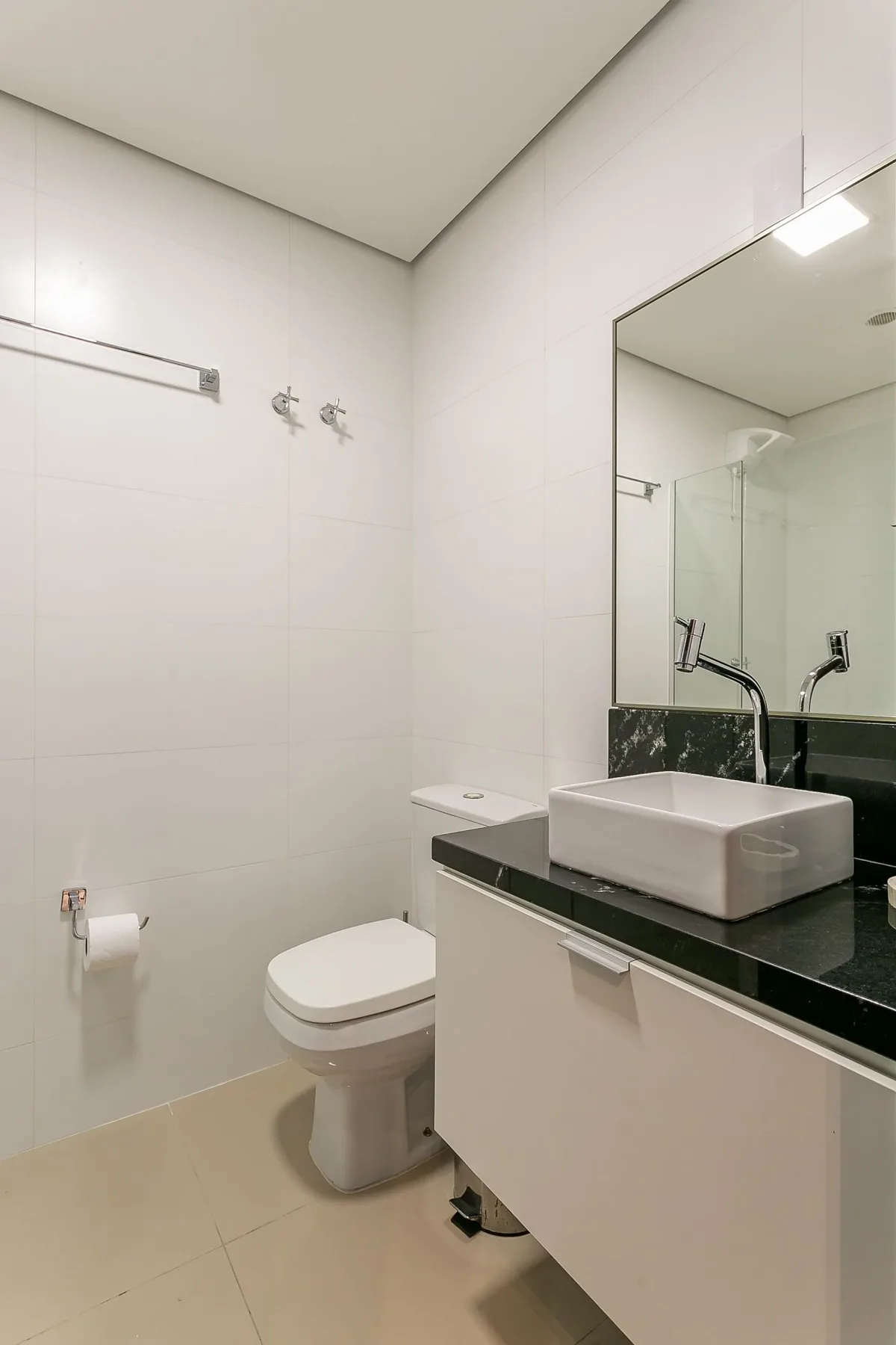 A tiled bathroom with a toilet and a sink beneath a large mirror.