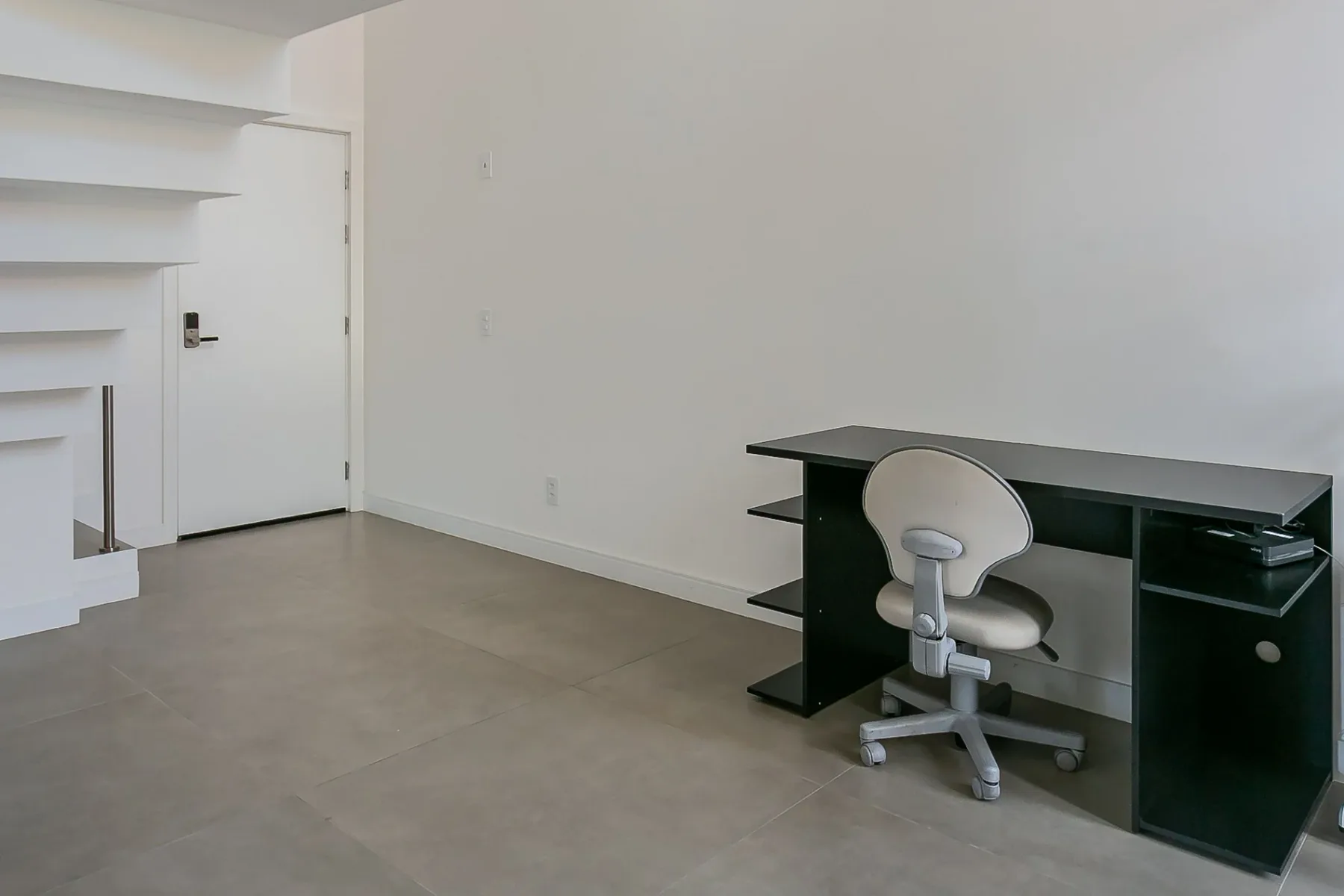 A simple room with a desk and rolling office chair against a bare wall.