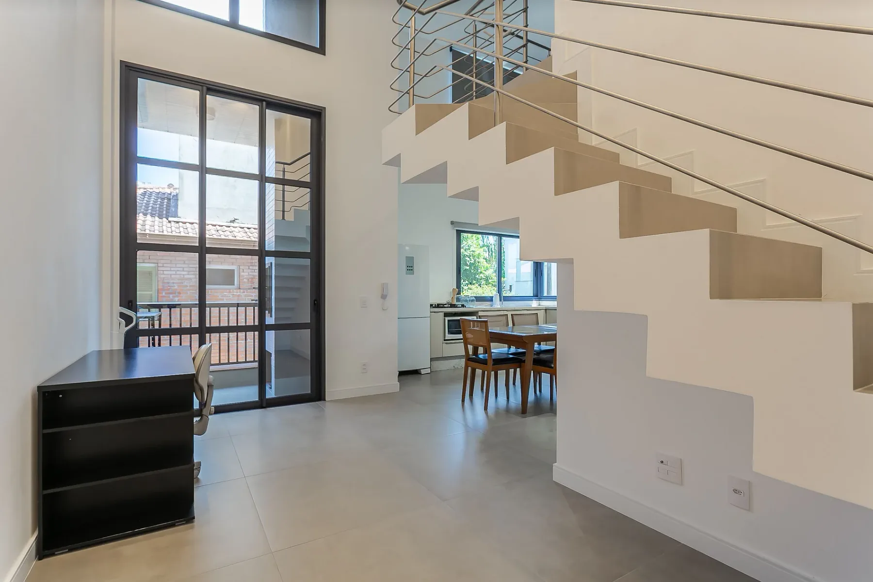 A bright open-plan room with a staircase and dining table beside the windows.