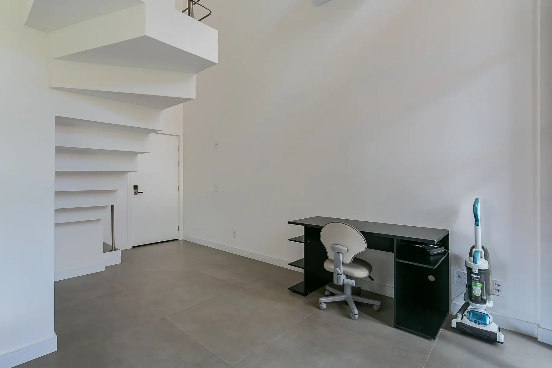 A bright room with a black desk and a vacuum cleaner.