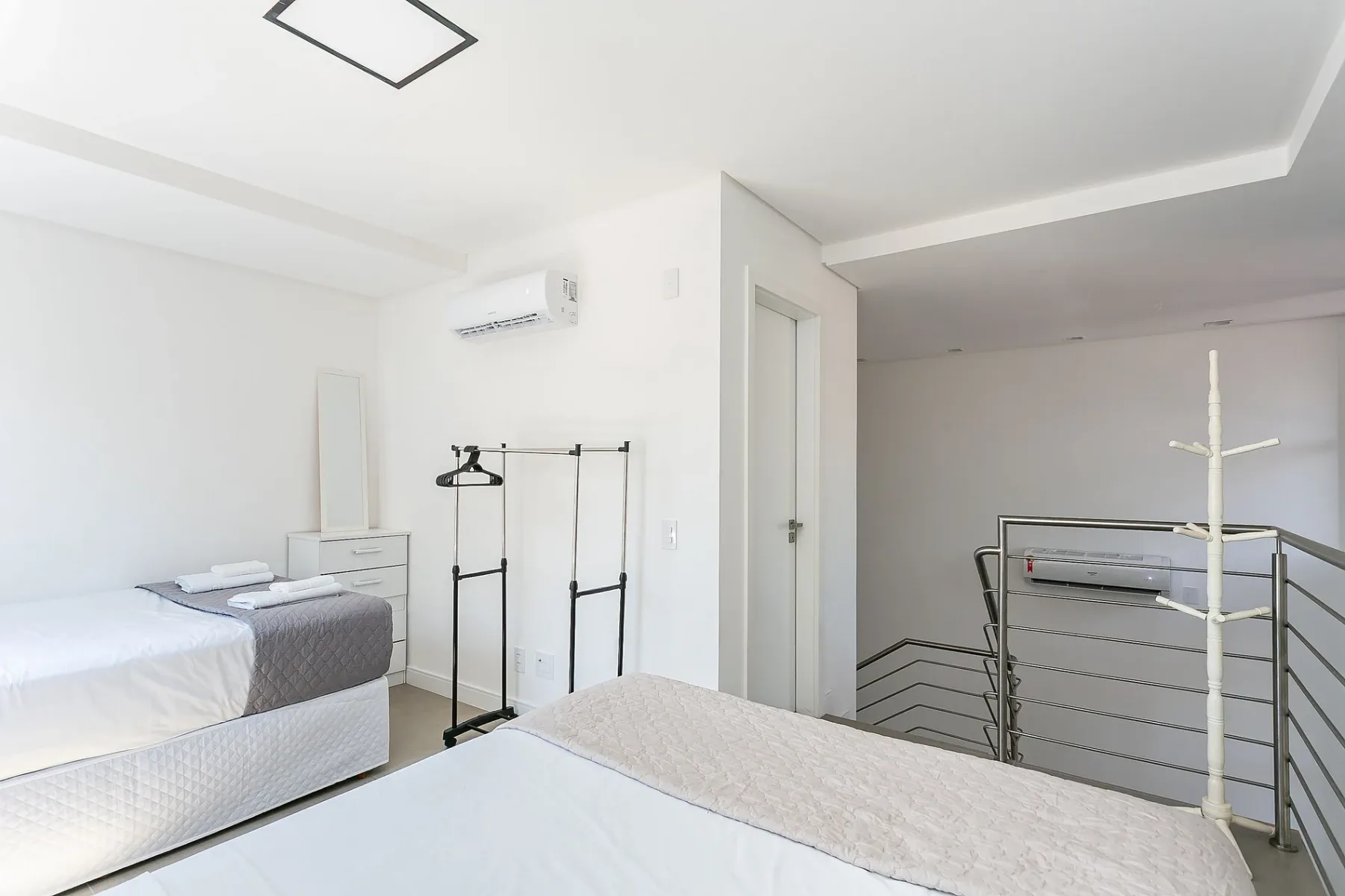 A bright bedroom with two beds and a clothes rack beside the doorway.