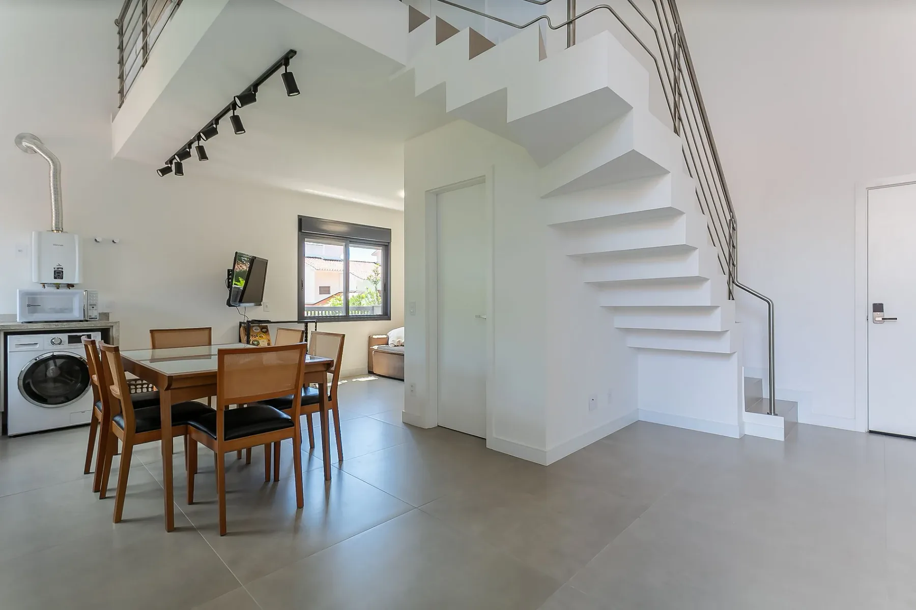 A dining area sits beneath a white staircase in a bright open room.