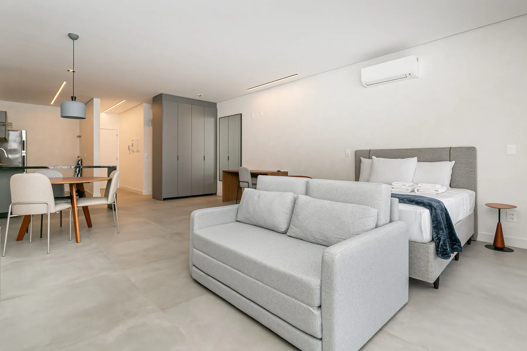 A bright studio room with a sofa, dining table, and bed.
