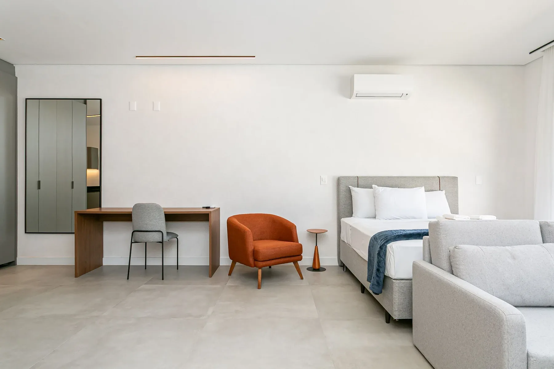 A bright bedroom with a bed, desk, and orange lounge chair.