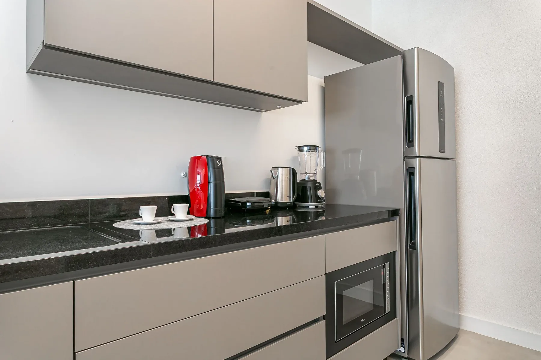 A modern kitchen with a dark countertop, small appliances, and a refrigerator.