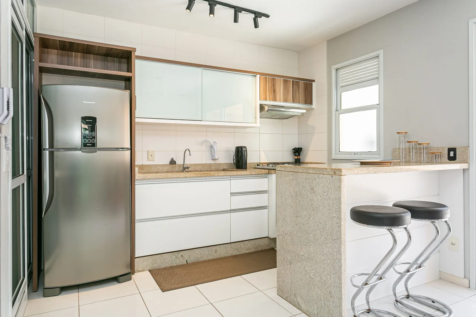 A bright kitchen with white cabinets, a stainless-steel refrigerator, and a small counter seating area.