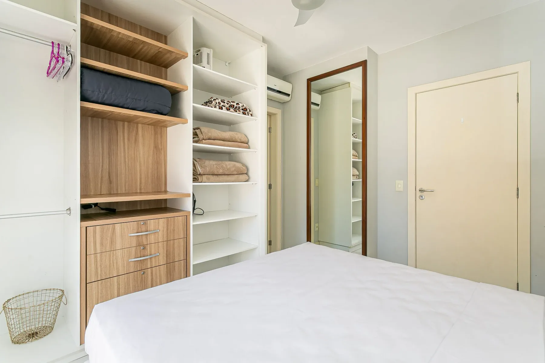 A bedroom with a bed and built-in shelving beside a mirrored wardrobe.