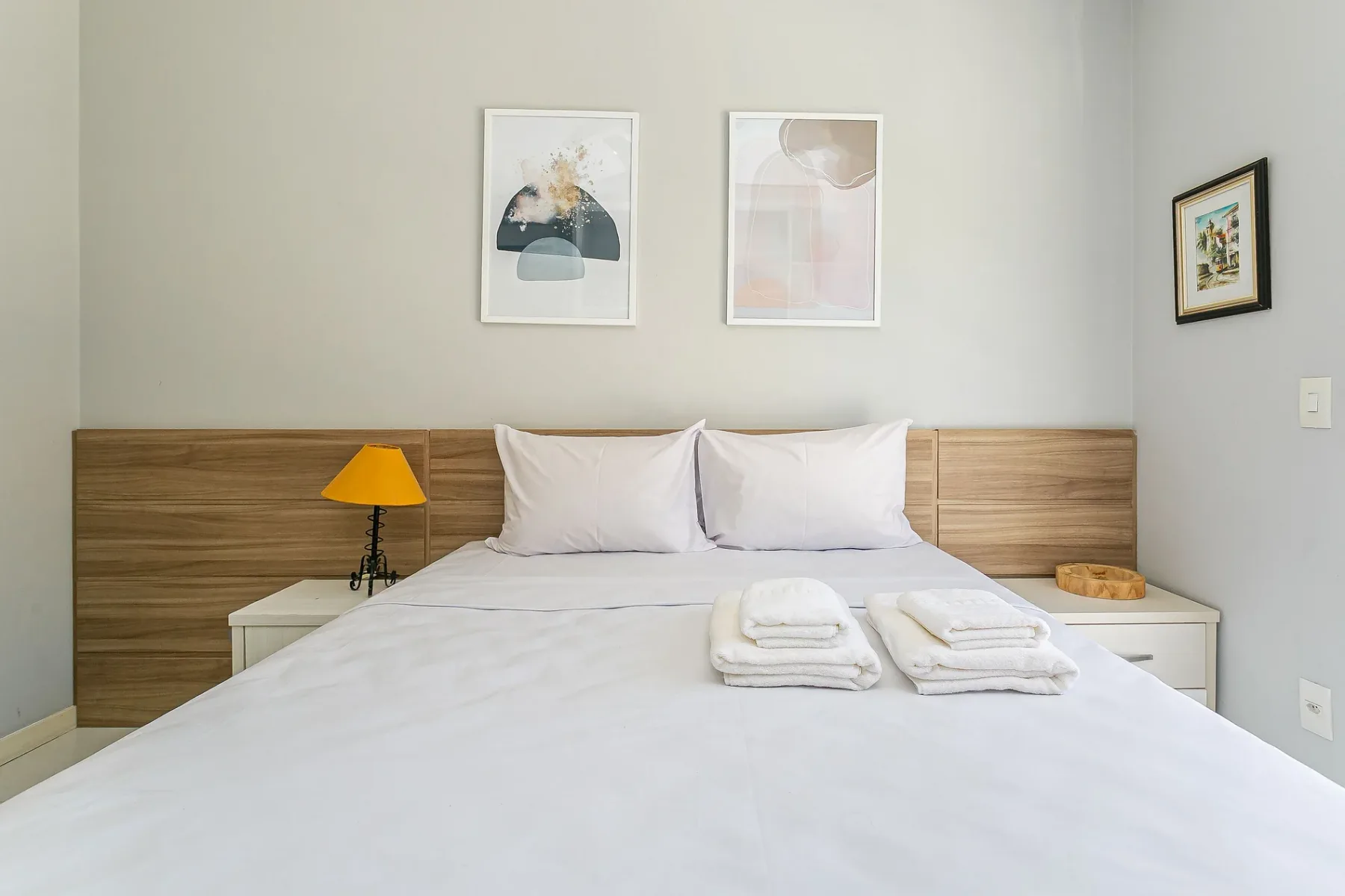 A bedroom with a neatly made bed and framed artwork above the headboard.