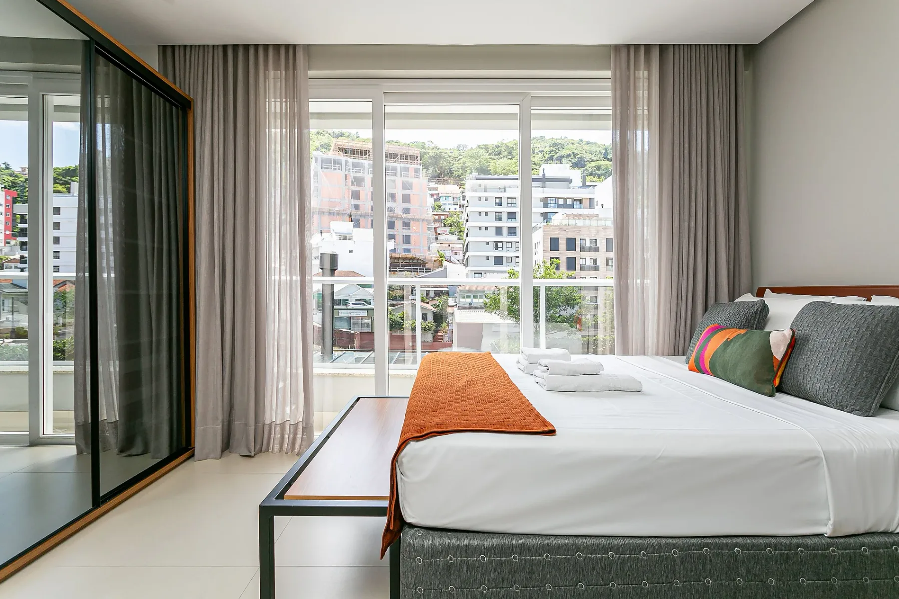 A bright bedroom with a large bed beside floor-to-ceiling windows.