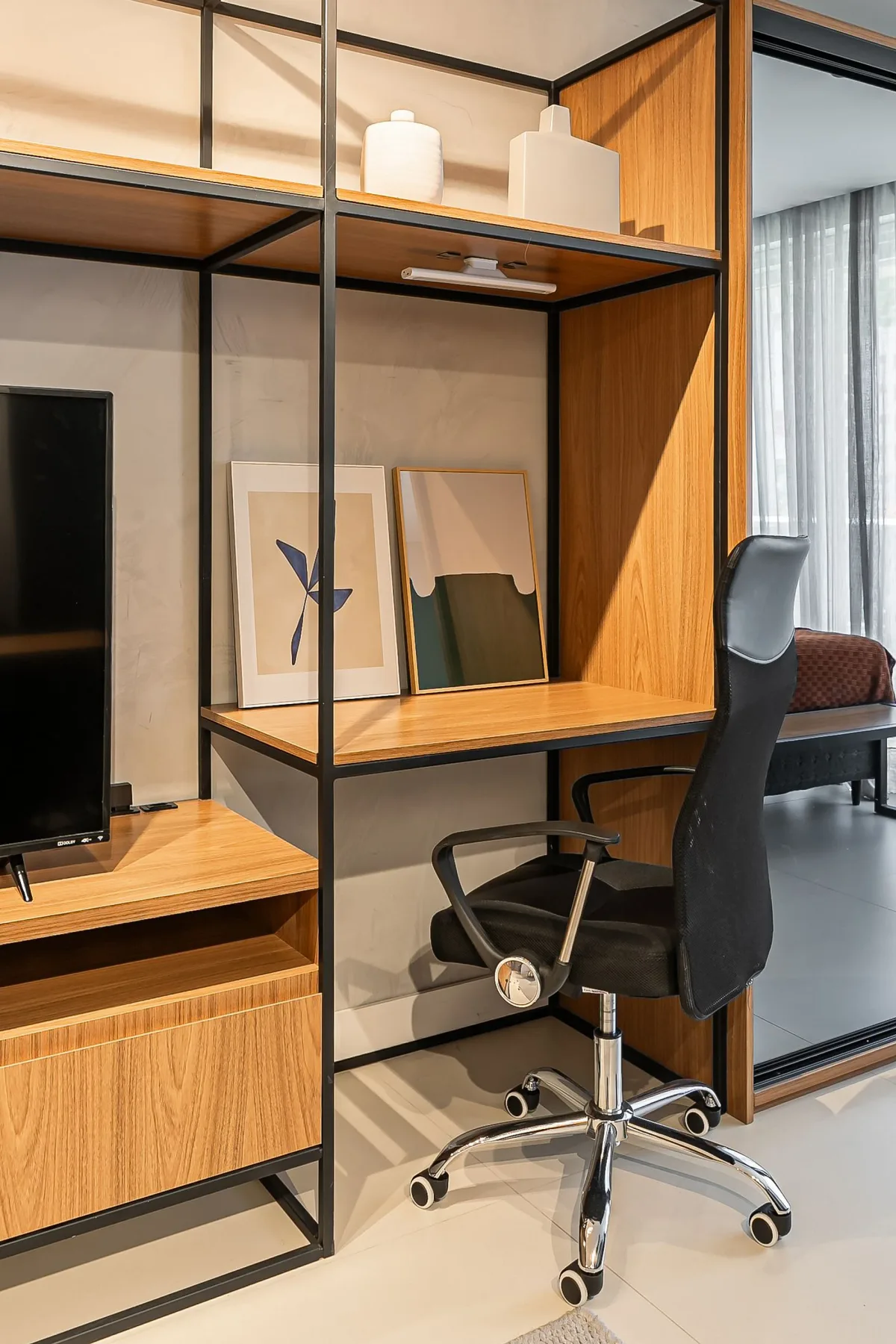 A desk and office chair sit beside shelving and framed artwork.
